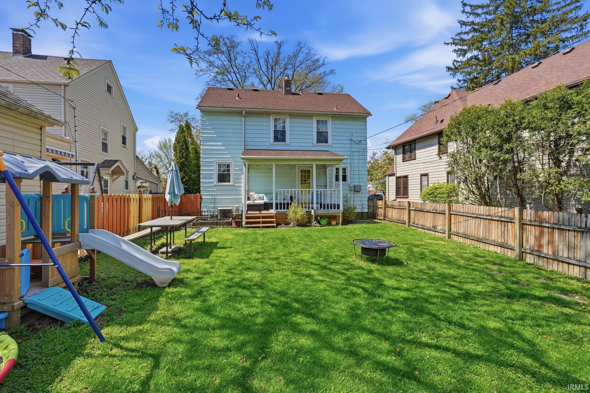 Expansive backyard featuring a manicured lawn, a full wooden privacy fence, and a covered porch with direct access to the interior