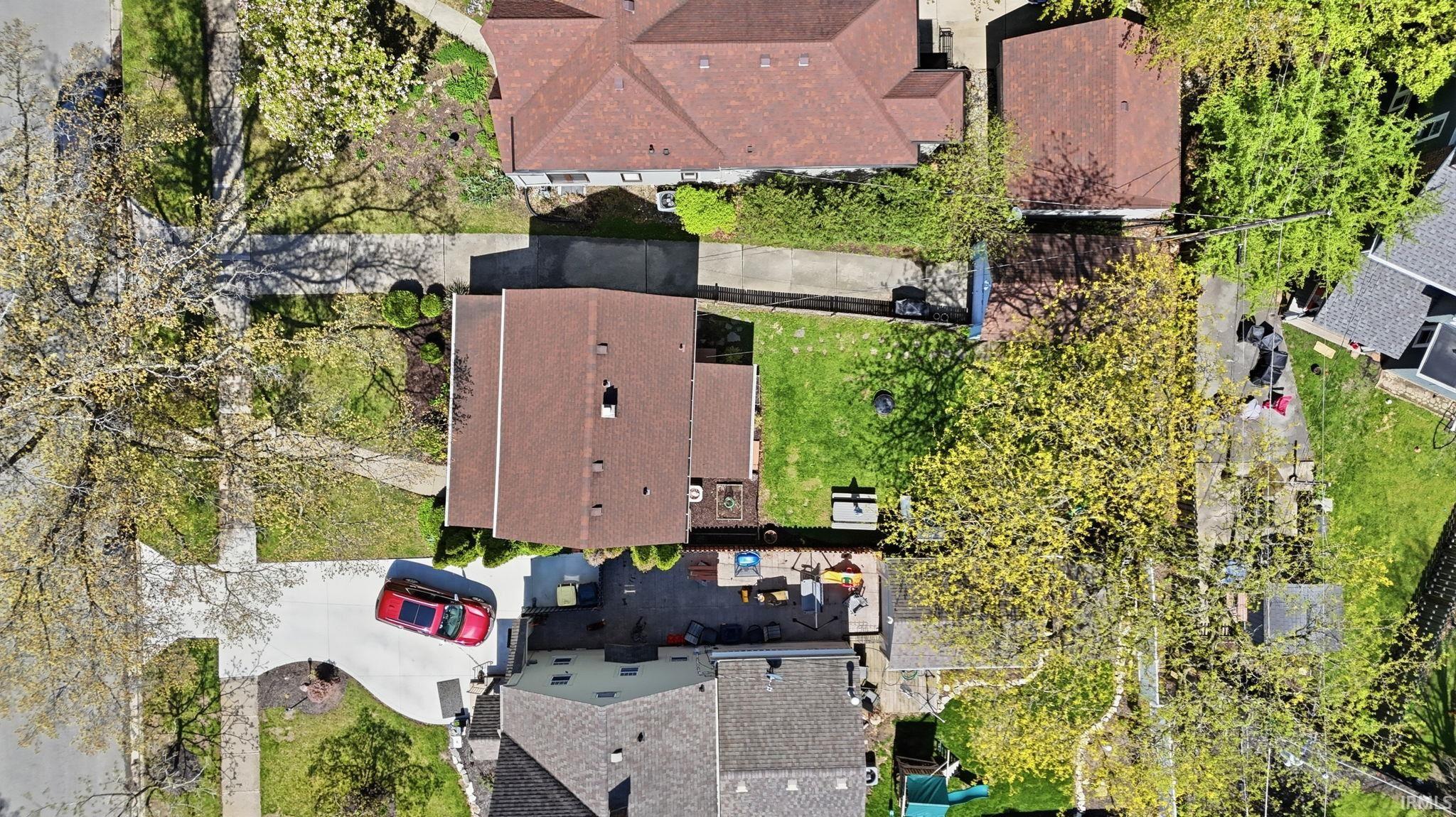 Aerial perspective showcasing the property with a brown shingle roof, a paved driveway, and a spacious green lawn