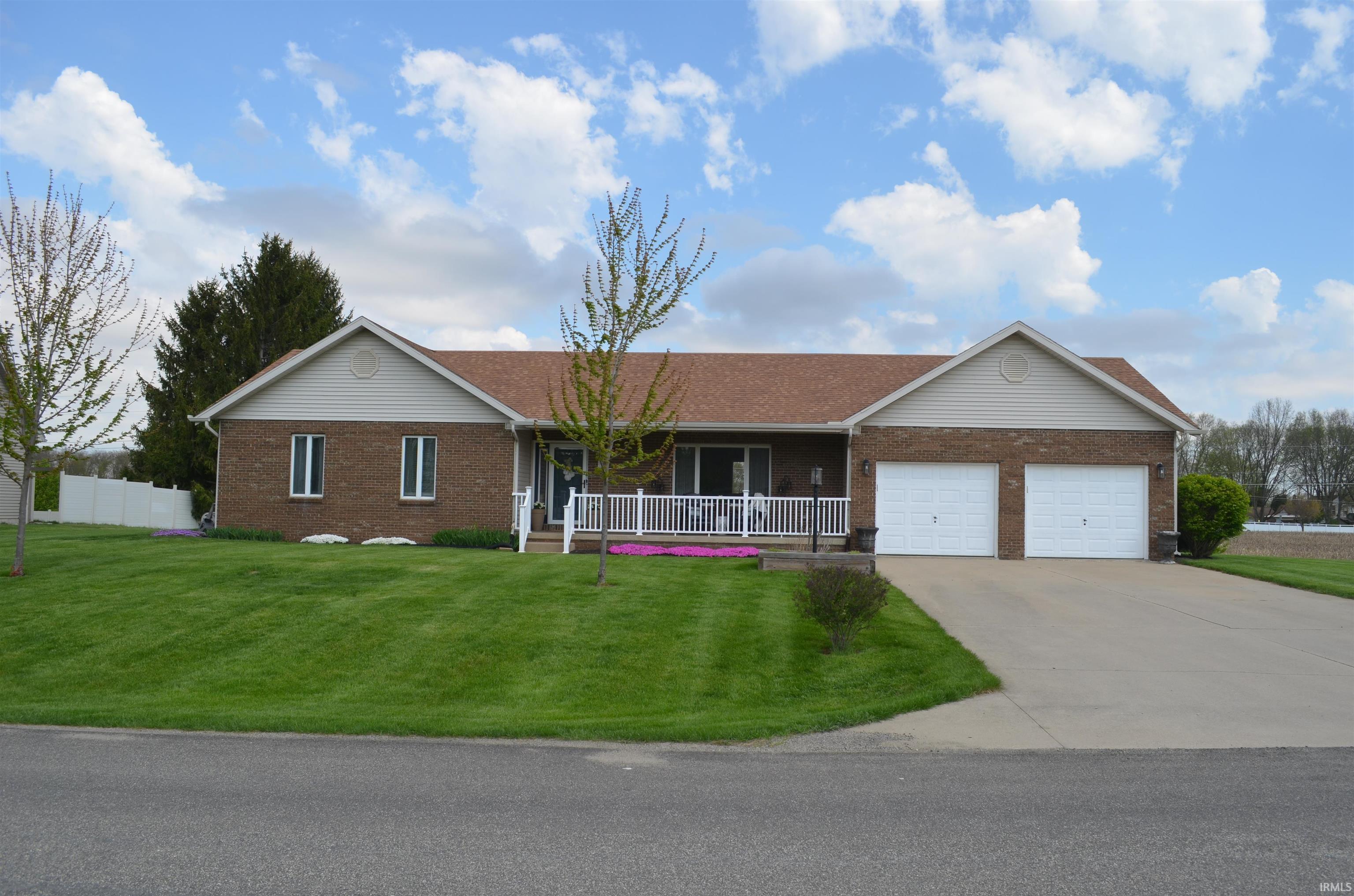 Brick facade residence featuring a two-car garage, mature landscaping, and a covered front porch with white railing