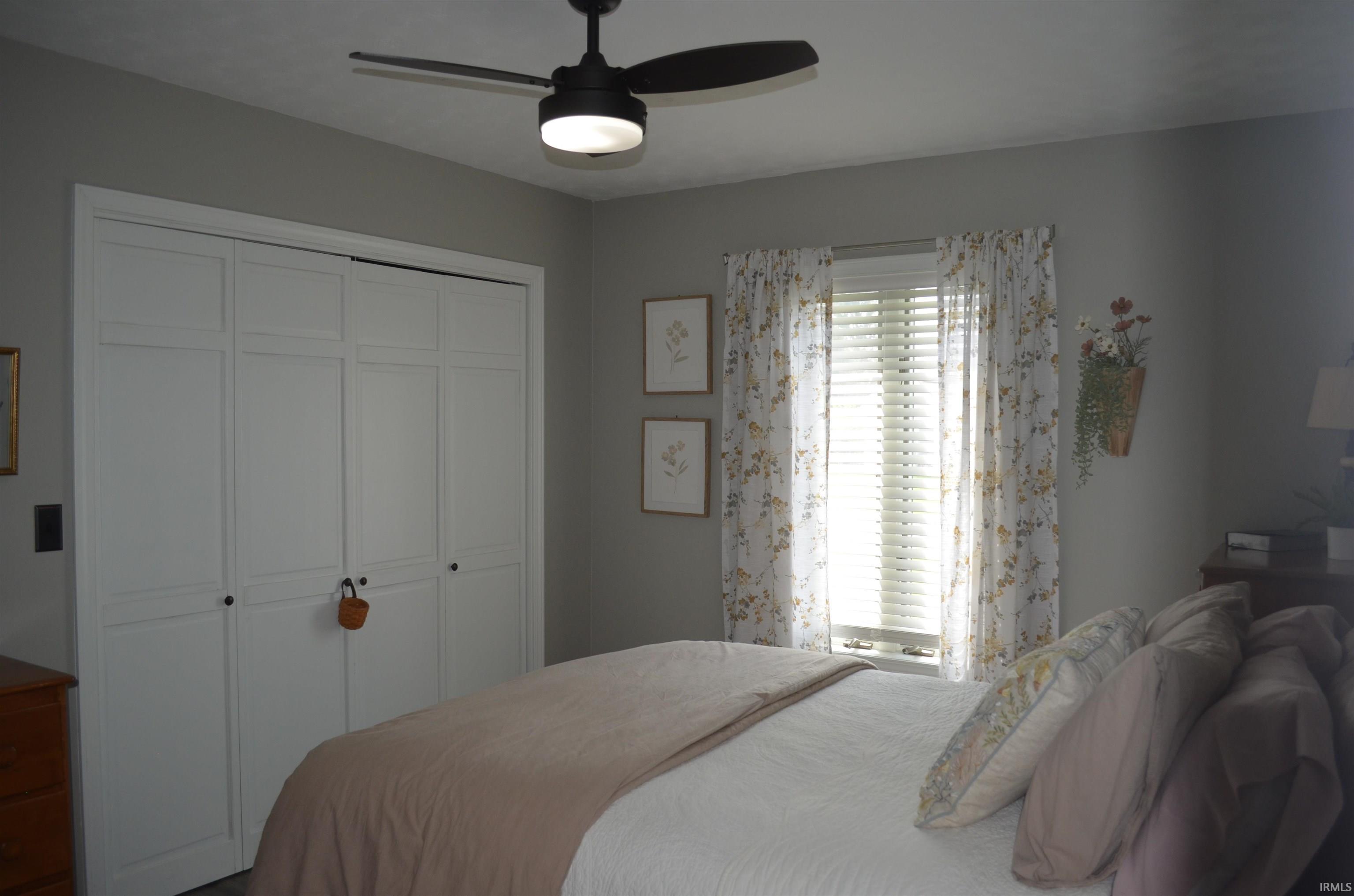 Bedroom featuring a ceiling fan with integrated lighting, white bi-fold closet doors, and a window with blinds
