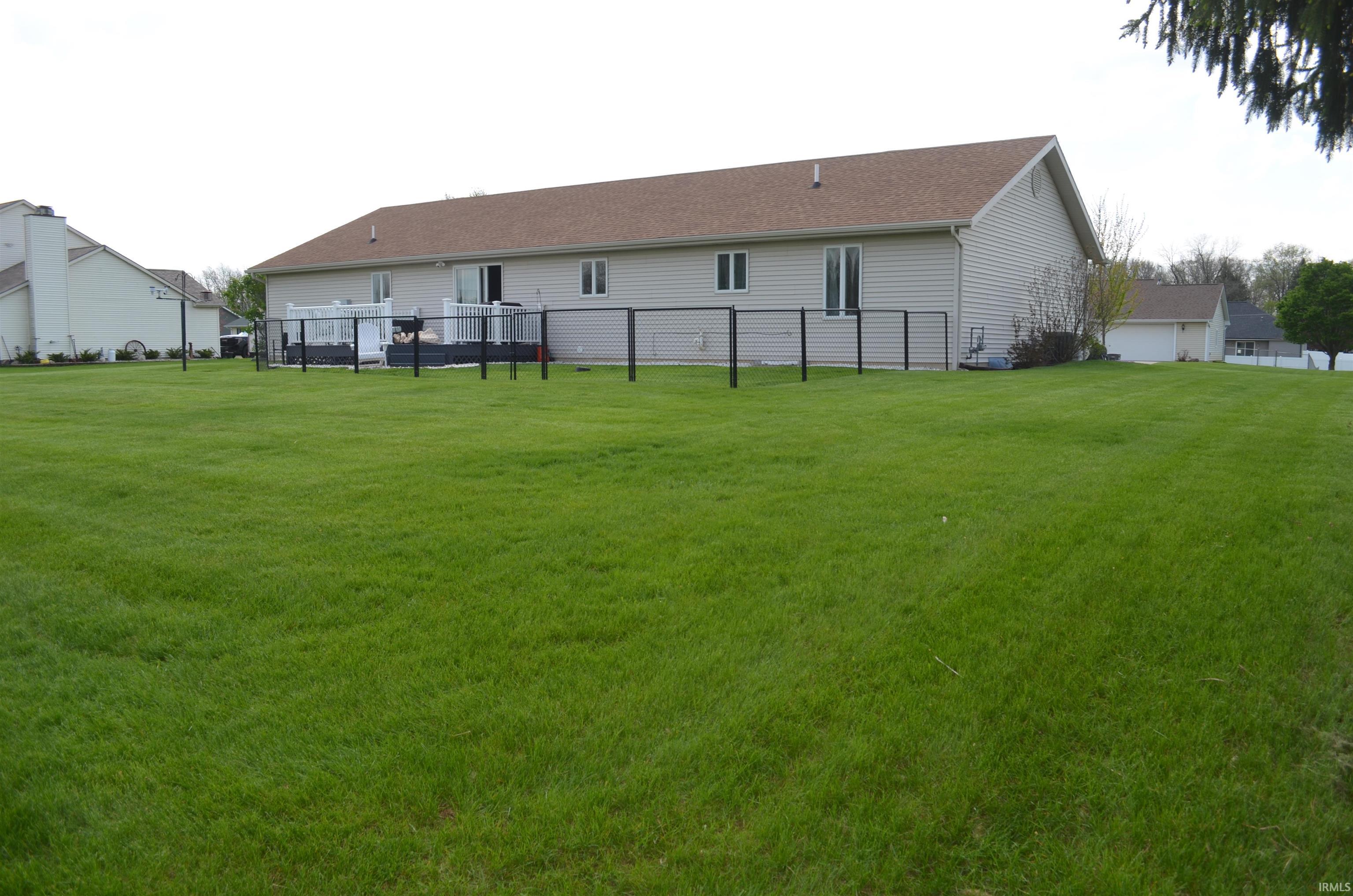 Expansive green lawn with a white vinyl-sided home featuring a brown shingle roof, a rear deck with a black metal fence, and sliding glass doors