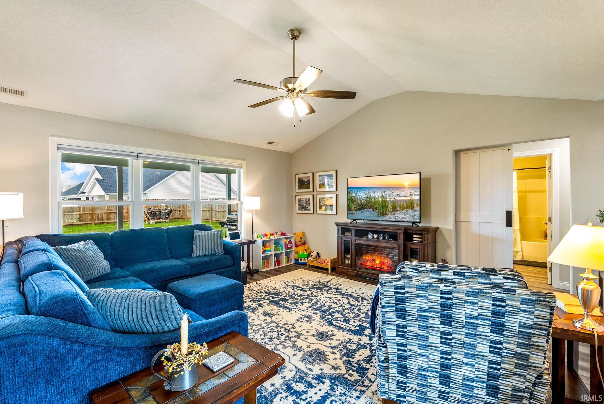 Living area featuring a vaulted ceiling with a ceiling fan, a wall of windows, and a built-in media console with an electric fireplace