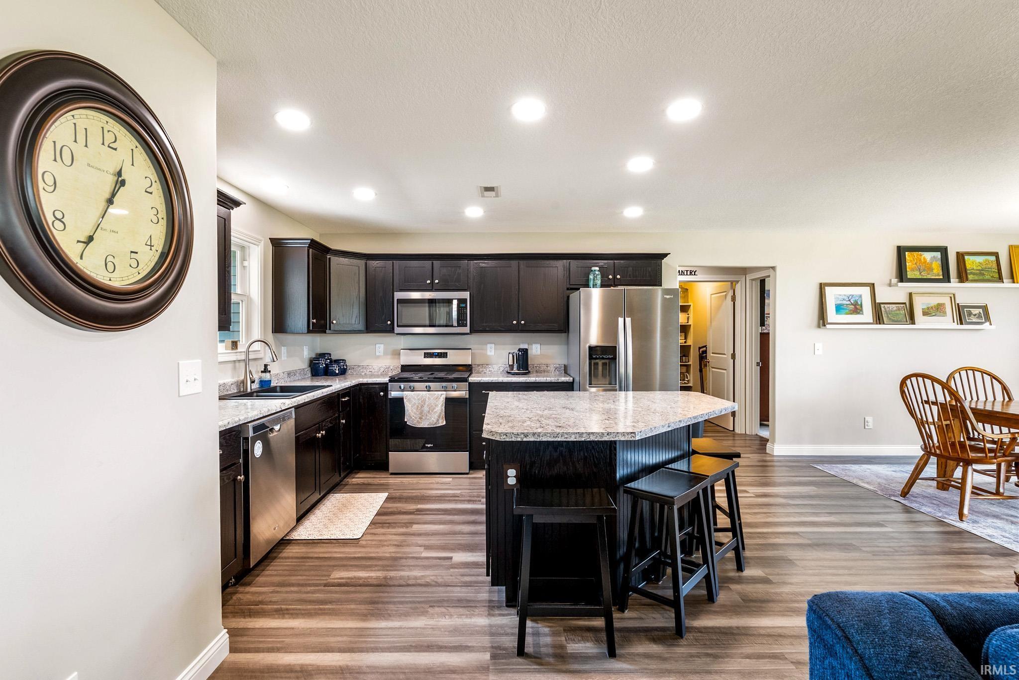 Open-concept kitchen featuring dark wood cabinetry, stainless steel appliances, speckled stone countertops, and a central island with bar seating