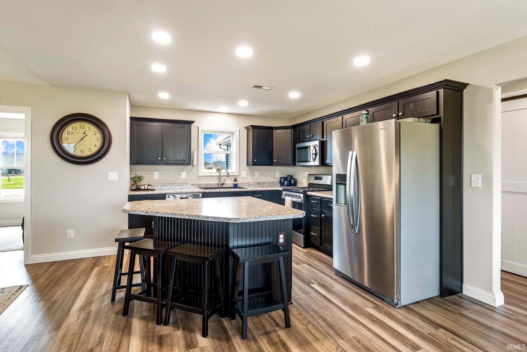 Kitchen featuring dark cabinetry, stainless steel appliances, and wood-finish flooring