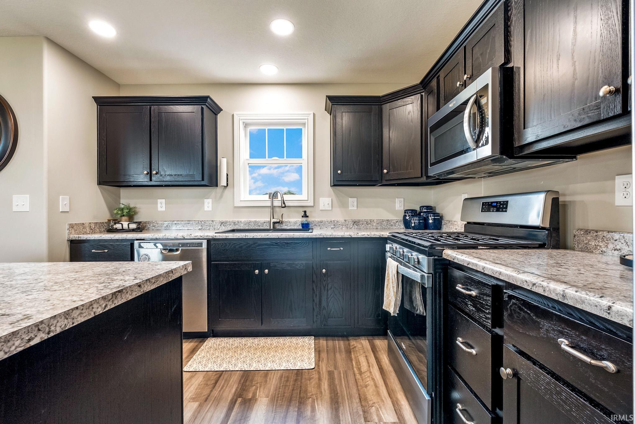 Kitchen featuring dark wood cabinetry, light speckled countertops, stainless steel appliances, and wood-finish flooring