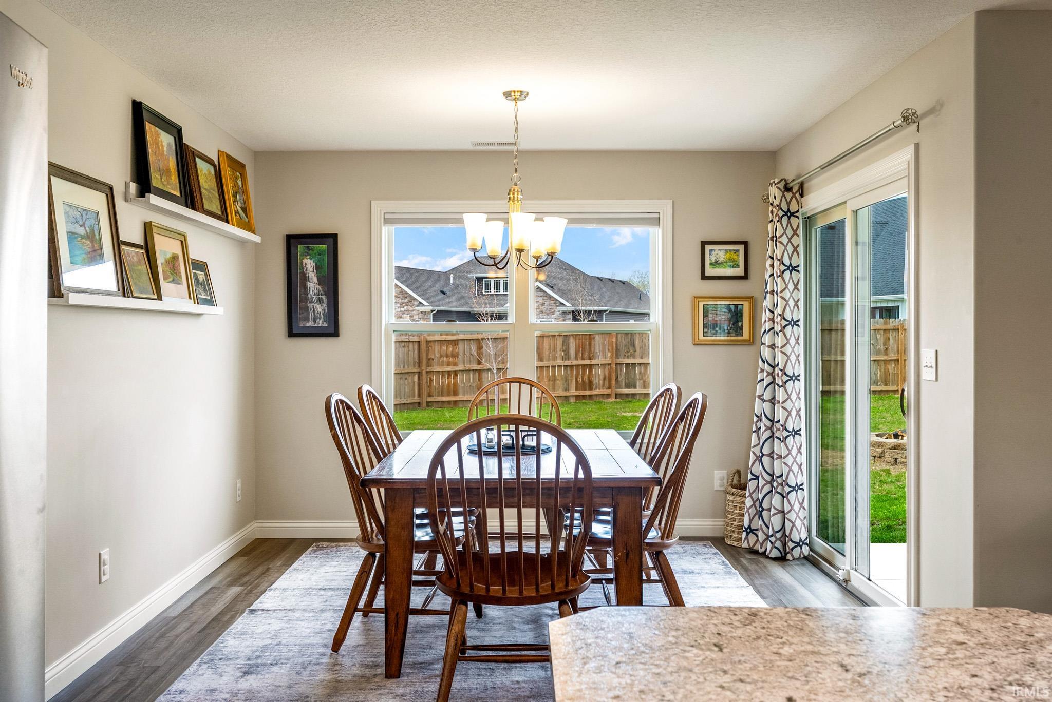 Dining area featuring wood-finish flooring, a contemporary chandelier, a window overlooking the backyard, and a sliding glass door providing outdoor access