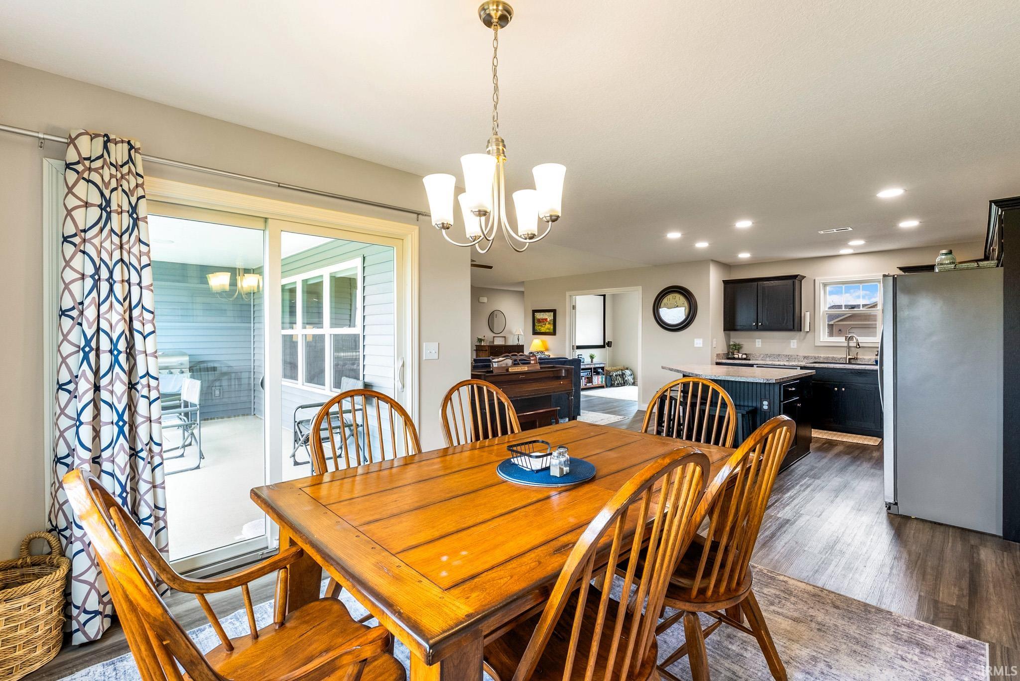 Open-concept dining area featuring a brass chandelier, wood-finish flooring, and recessed lighting