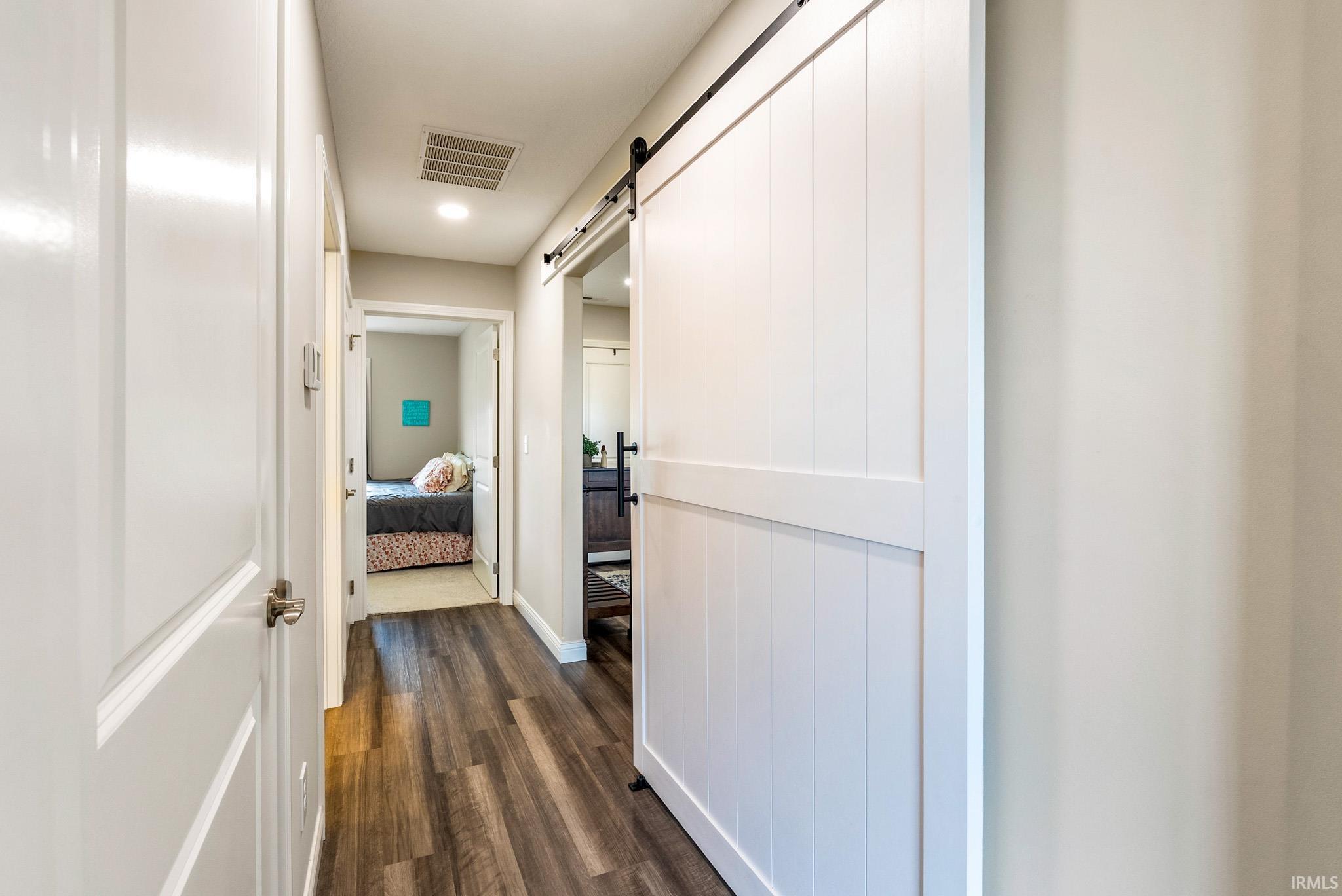 Hallway featuring wood-finish flooring, recessed lighting, white interior doors, and a white barn door with black hardware