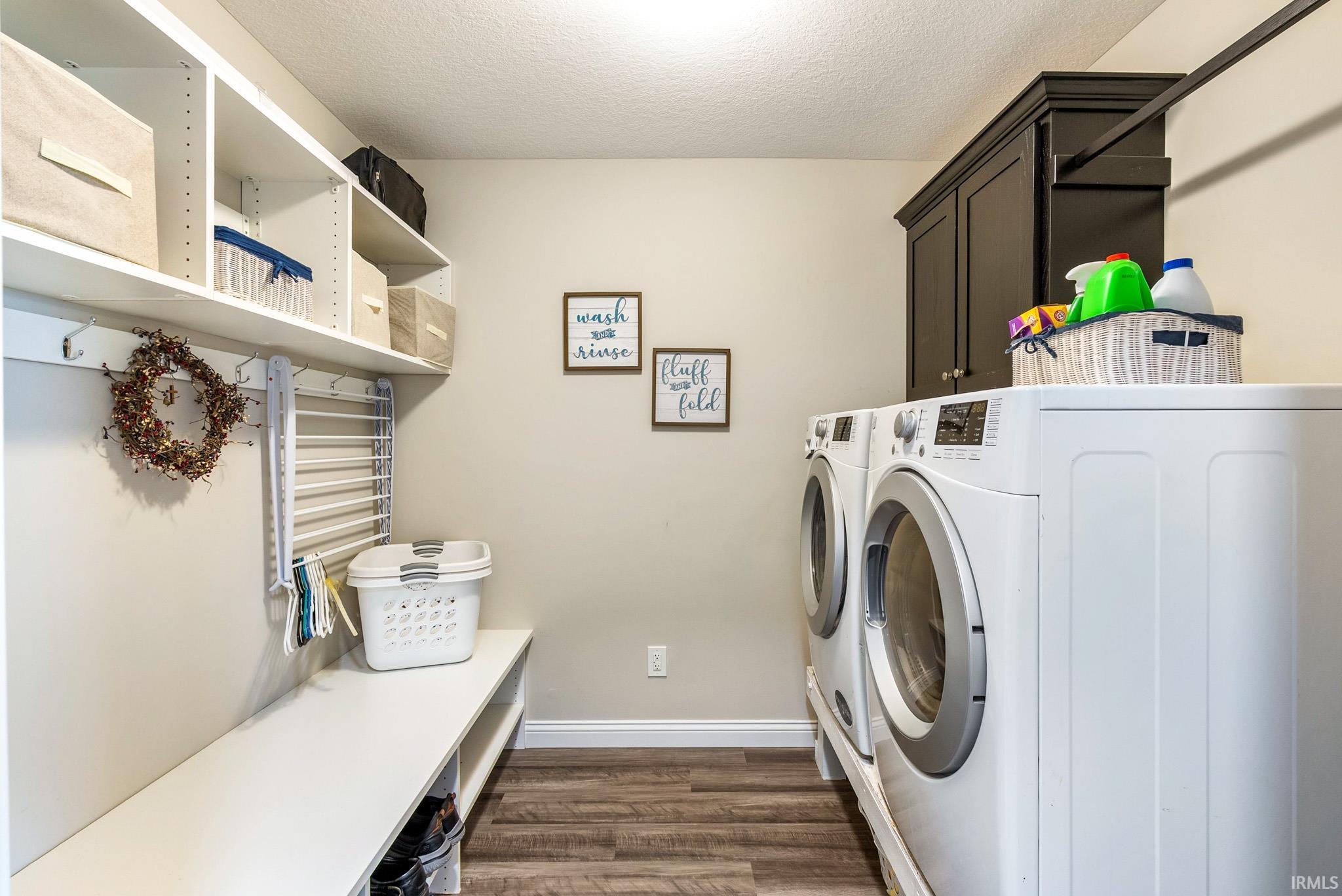 Functional laundry space featuring front-loading appliances, dark cabinetry, and wood-finish flooring