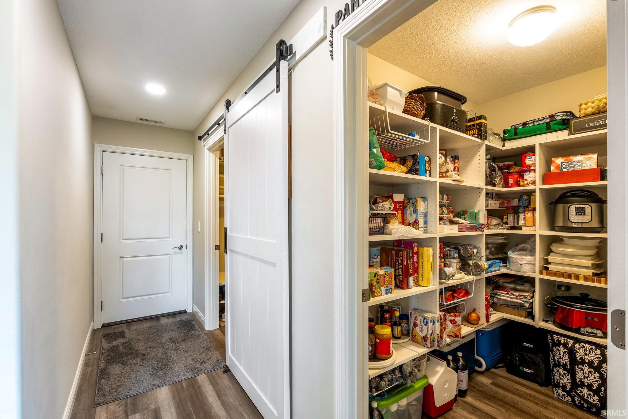 Spacious walk-in pantry with extensive shelving, wood-finish flooring, and a flush mount ceiling light