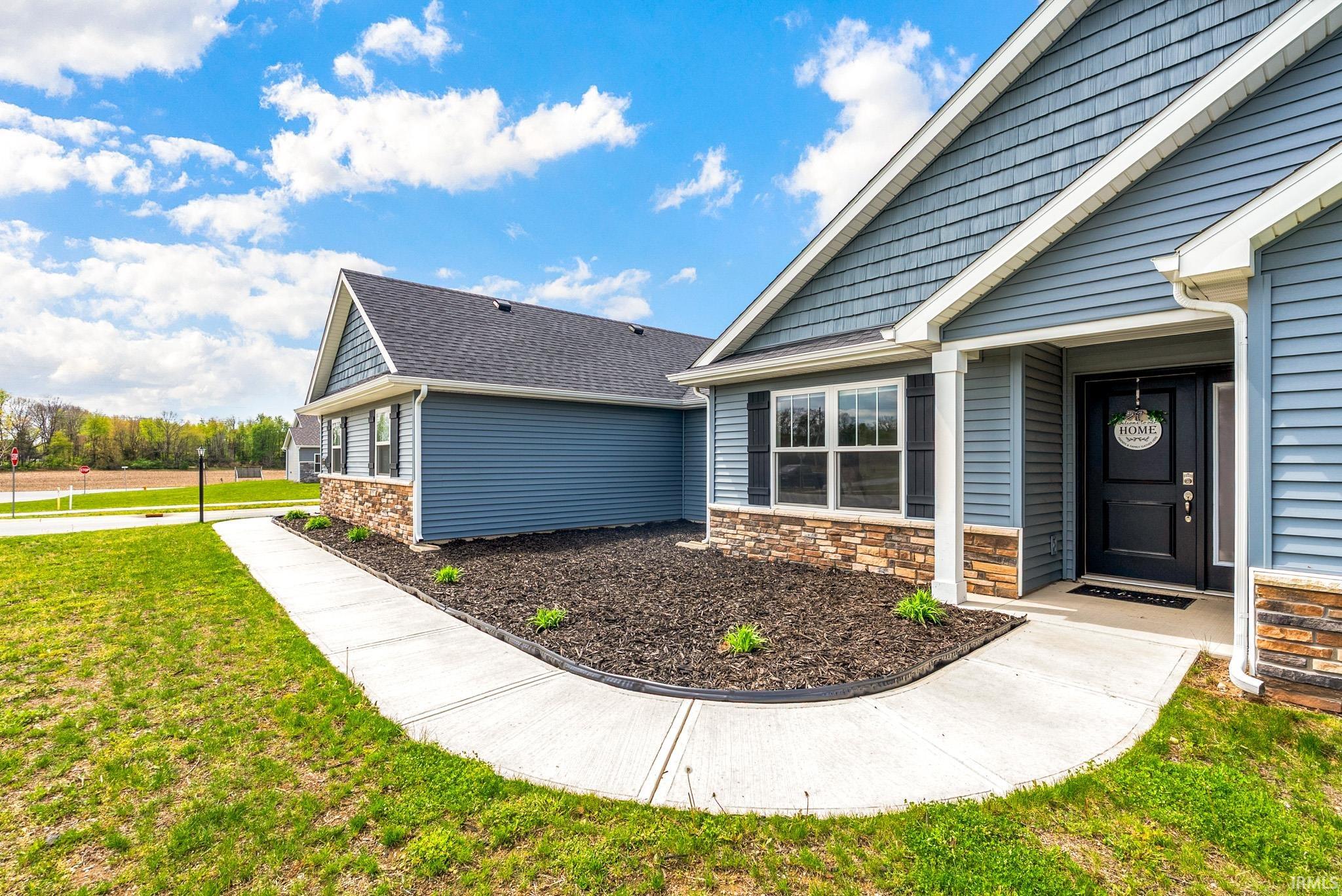 Contemporary exterior featuring blue horizontal siding, dimensional shingle roofing, stone veneer accents, a covered entry, and a concrete walkway
