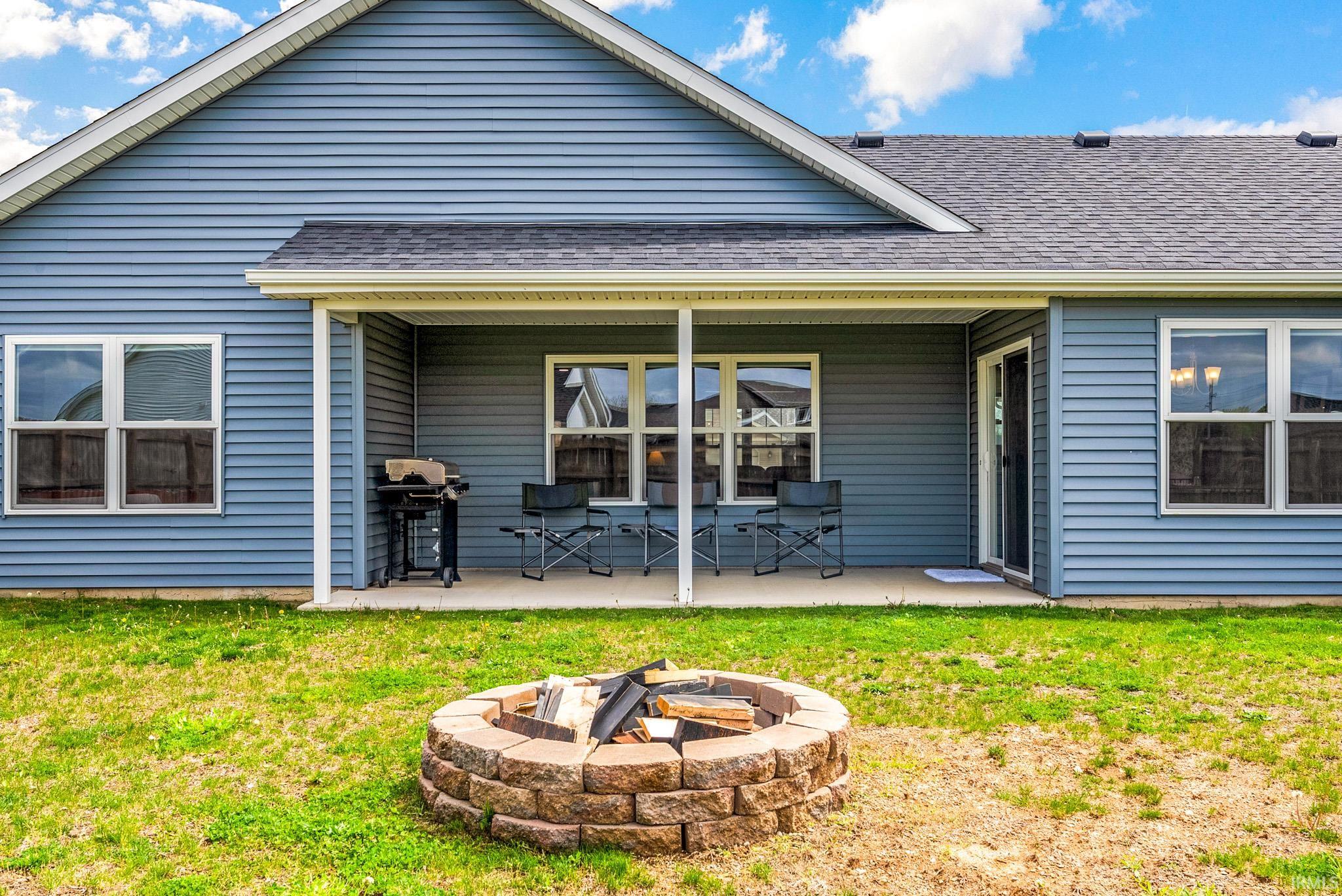 Rear exterior showcasing blue vinyl siding, an exposed aggregate patio, and a stone fire pit