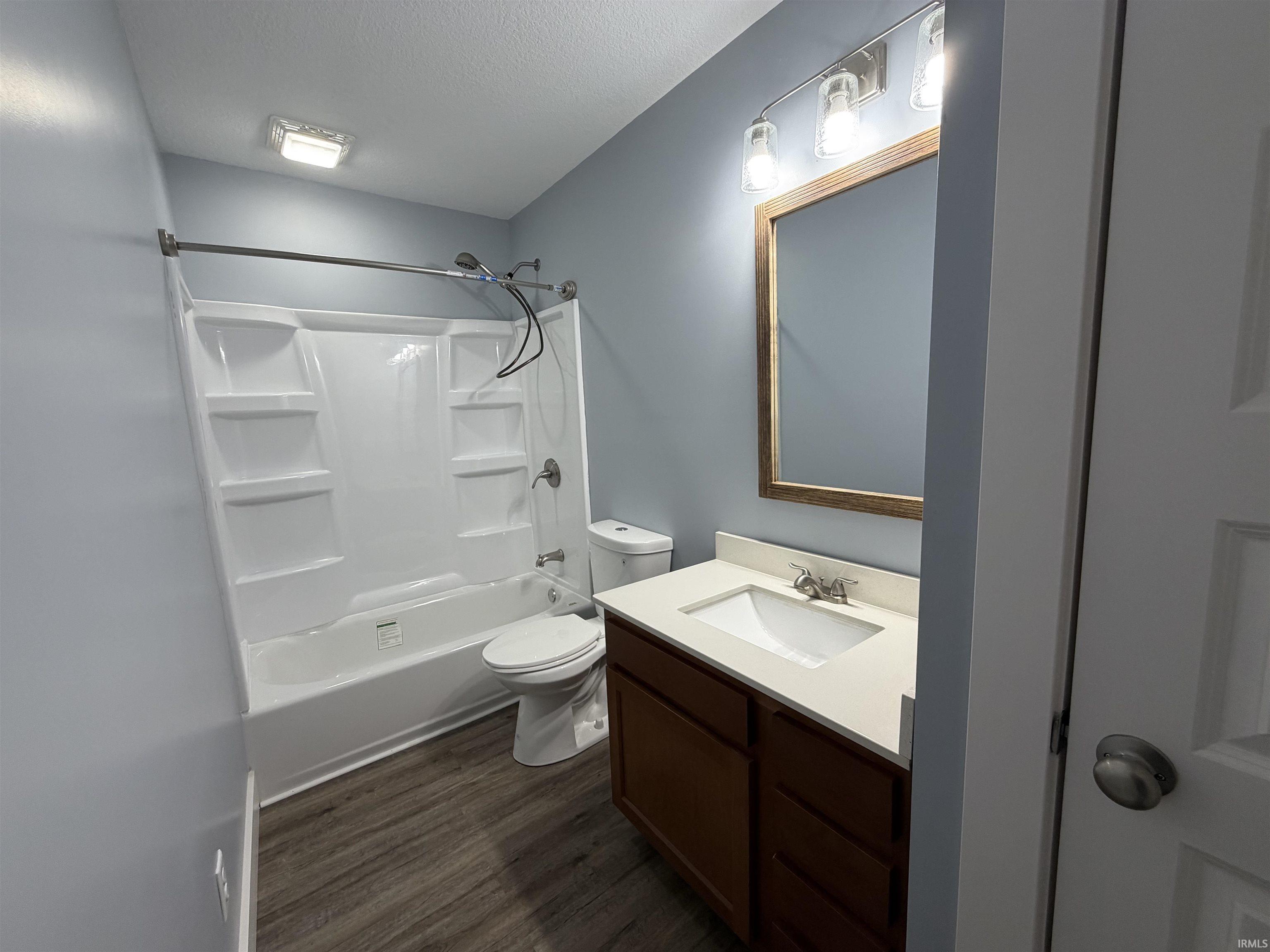 Bathroom with vanity, bathtub / shower combination, dark wood-type flooring, and a textured ceiling