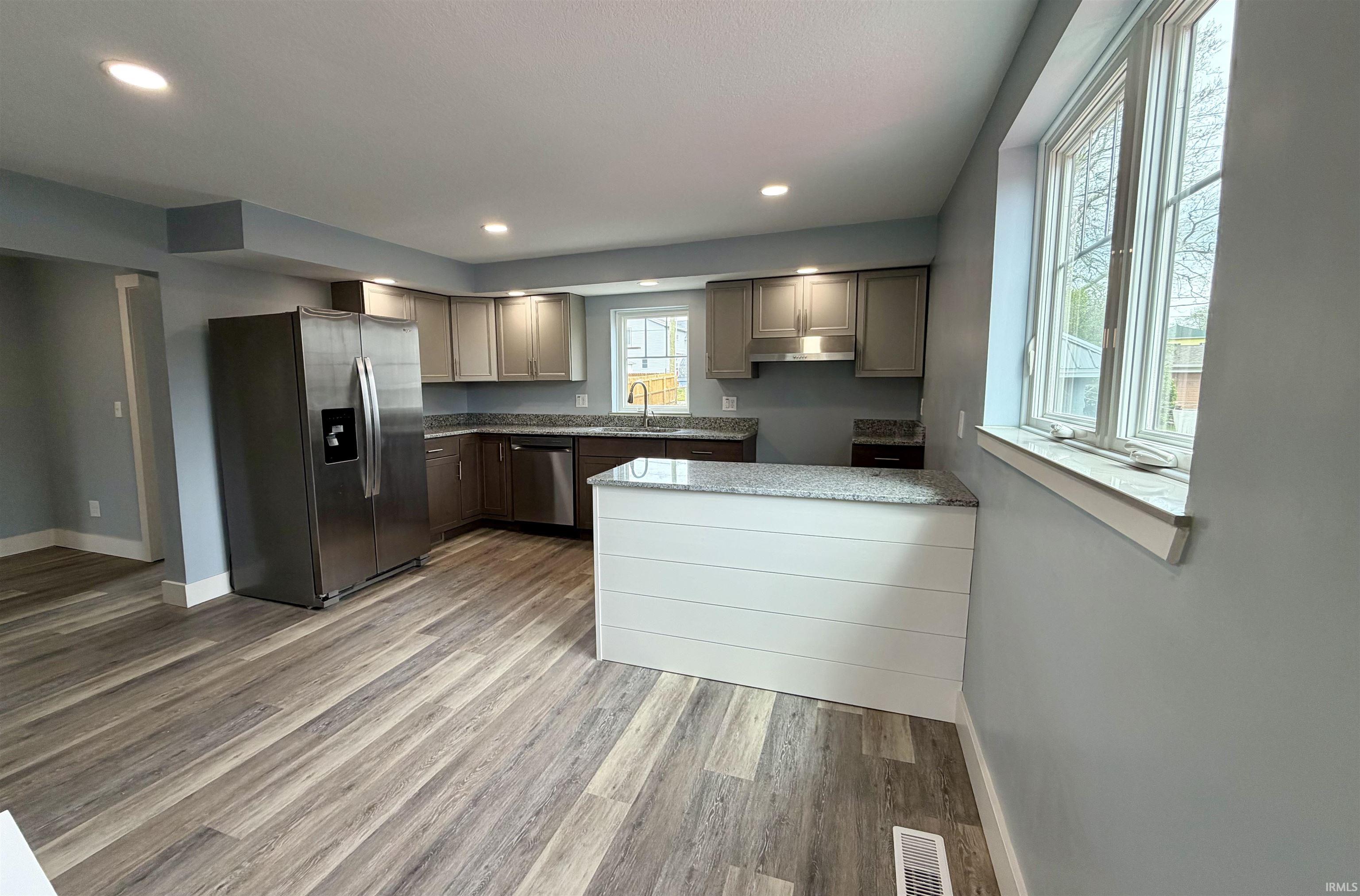 Kitchen featuring stainless steel appliances, light wood finished floors, a peninsula, light stone countertops, and recessed lighting