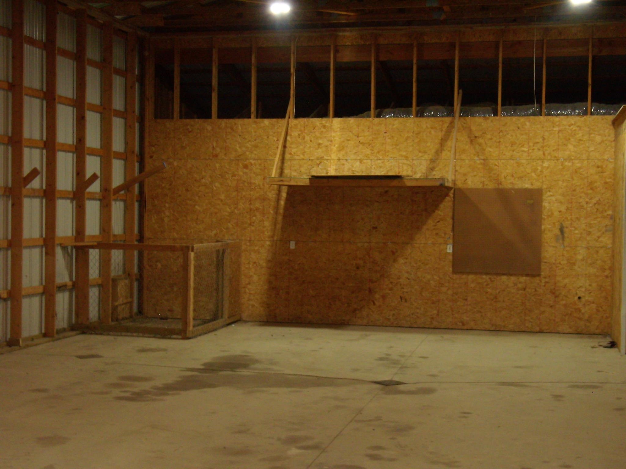 Spacious interior featuring concrete flooring, partial wood paneling, exposed ceiling joists, and overhead lighting