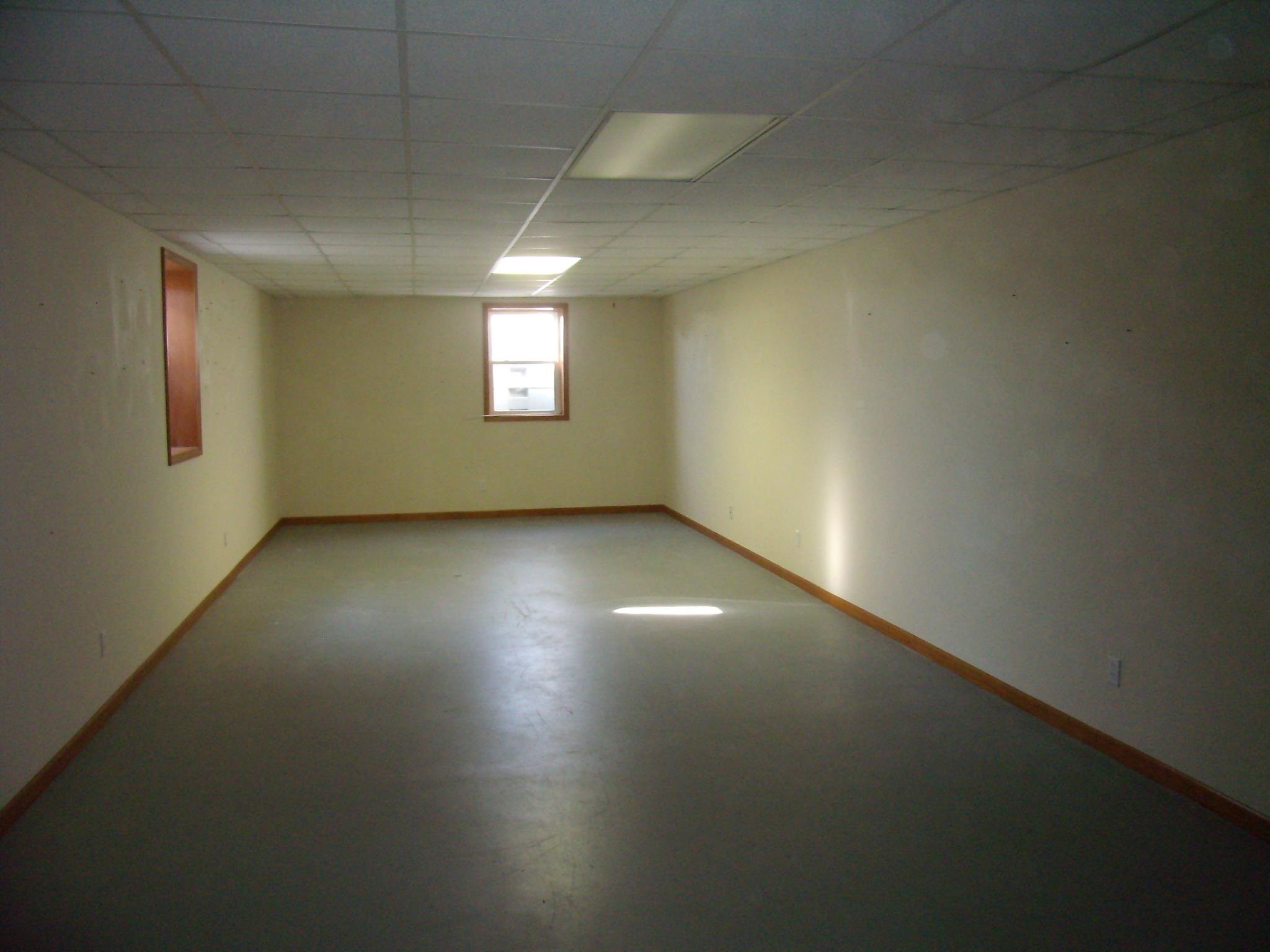 Spacious room featuring light-toned walls, wood trim, and a drop ceiling with integrated lighting