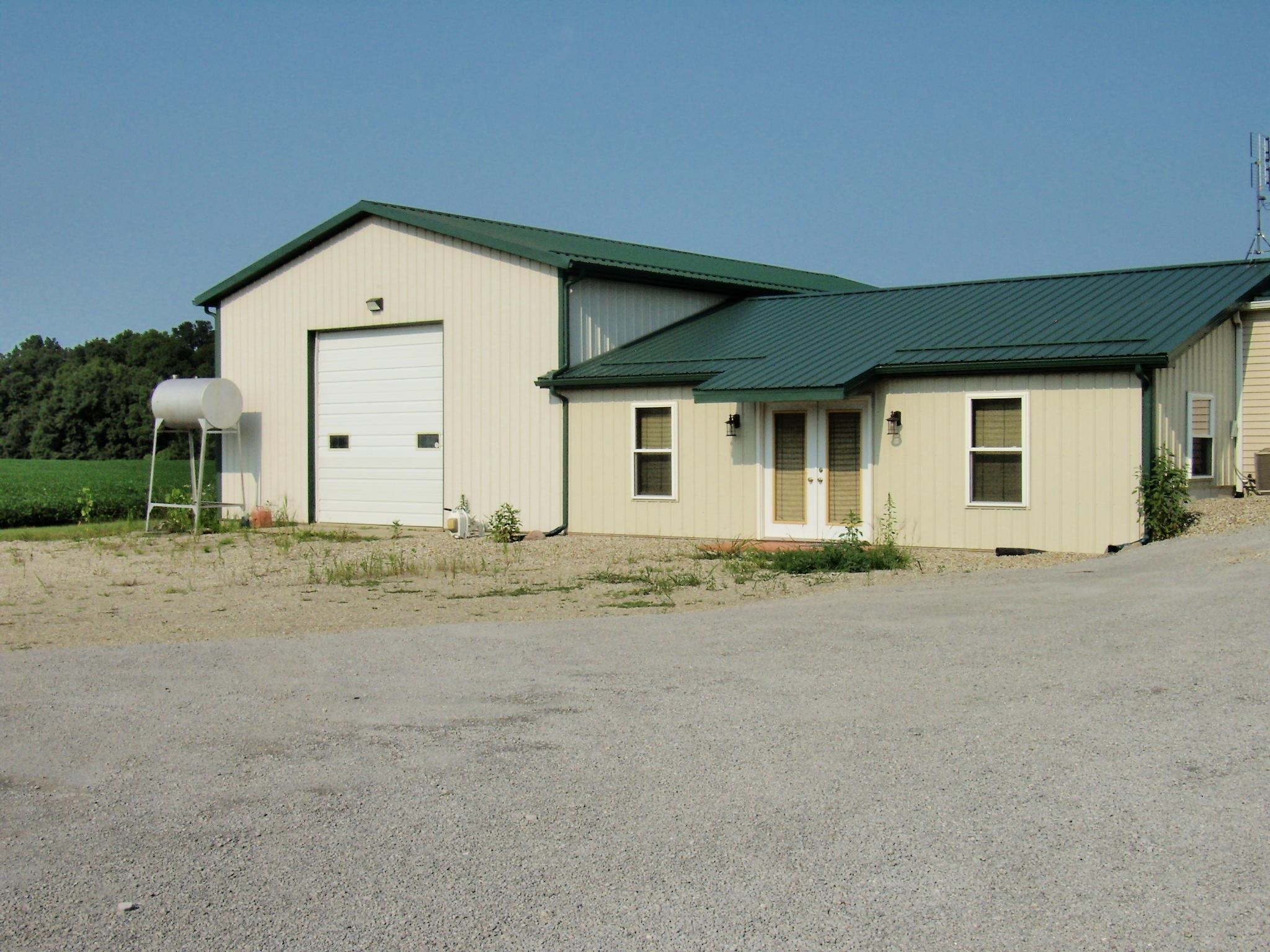 Light-colored siding structure with a green metal roof and an integrated garage featuring a white overhead door