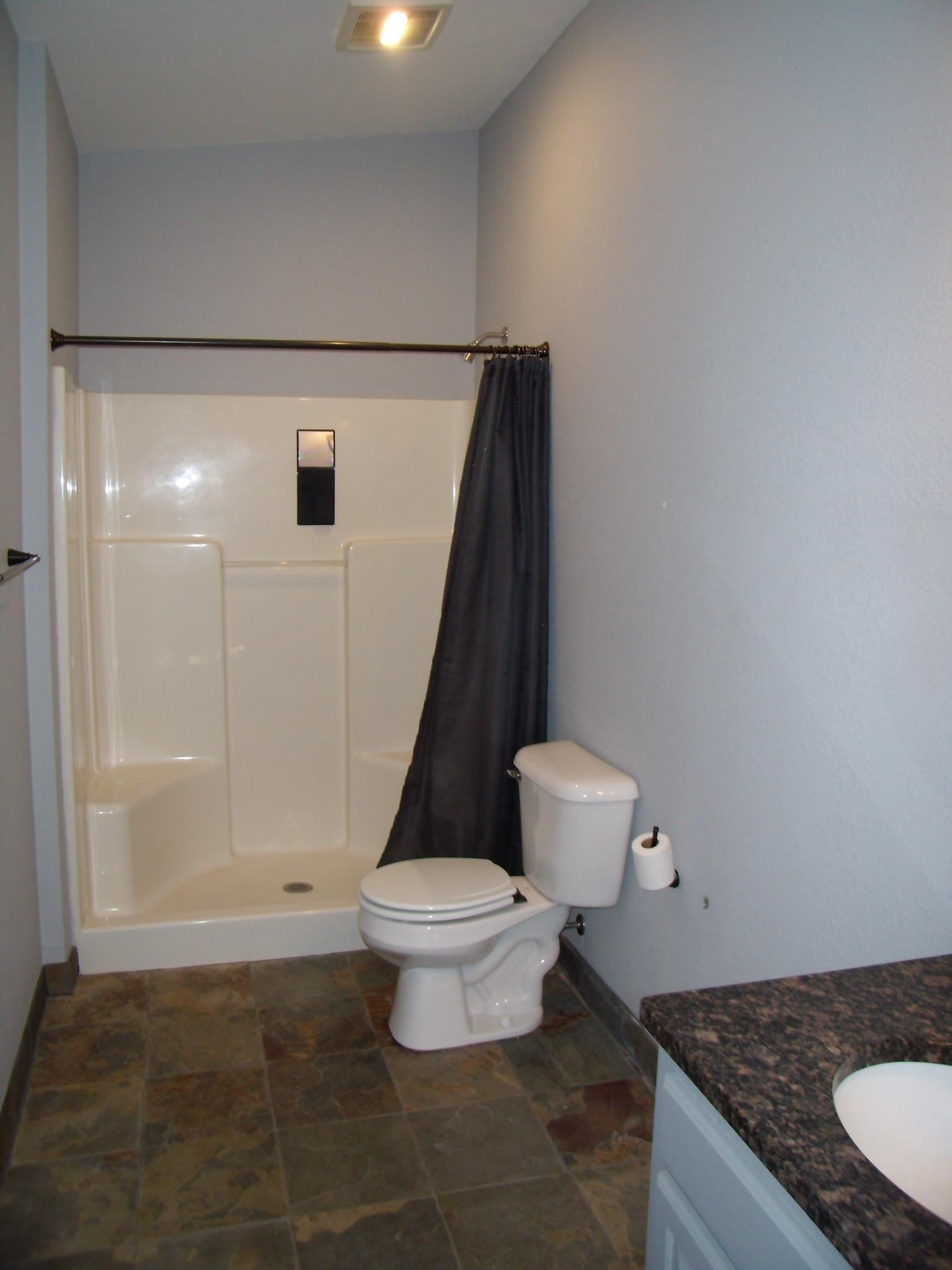 Bathroom featuring a white shower stall with a dark shower curtain, a white toilet, and a vanity with a dark countertop and undermount sink