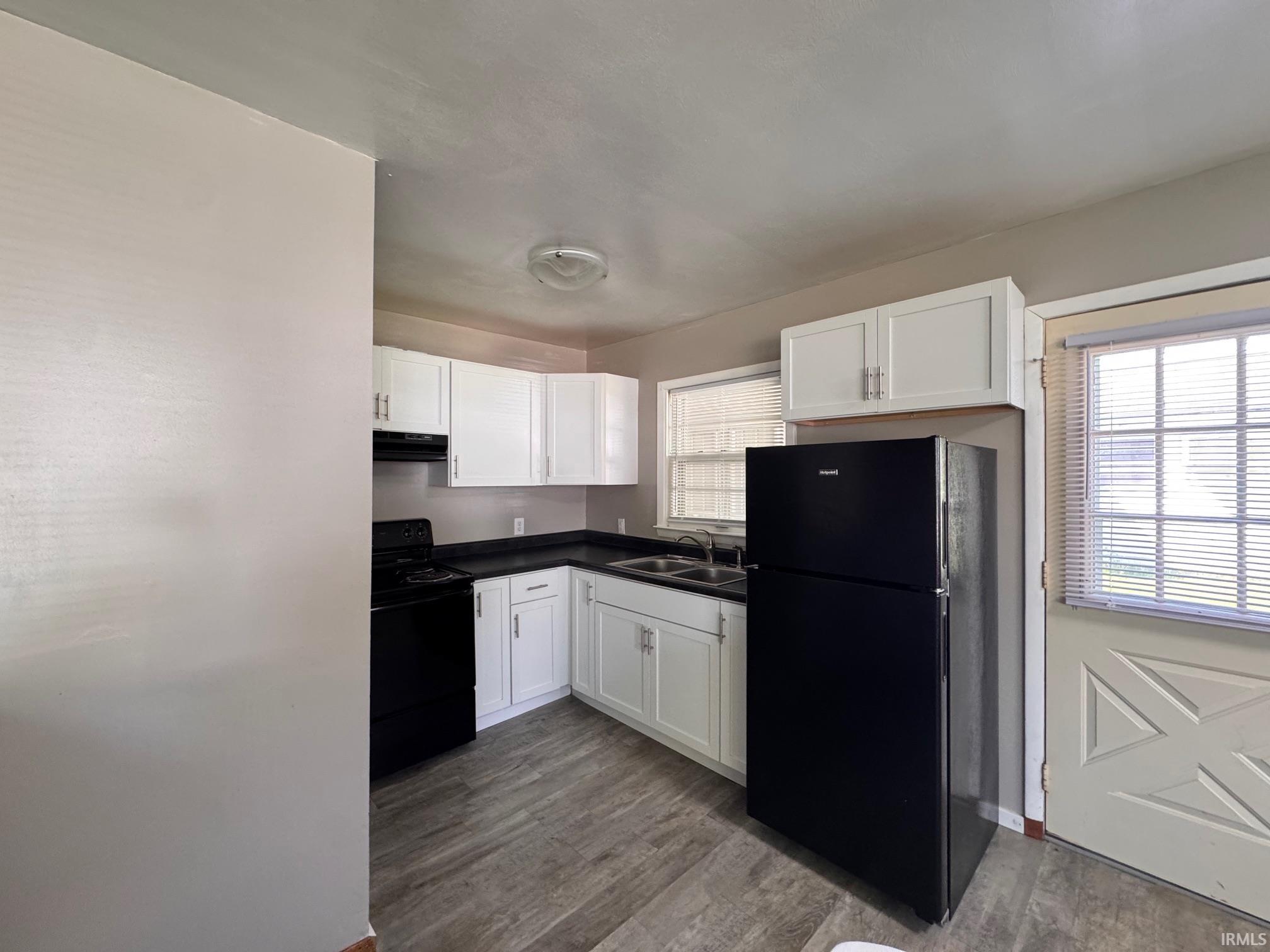 Kitchen featuring wood-finish flooring, white cabinetry, black countertops, and black appliances
