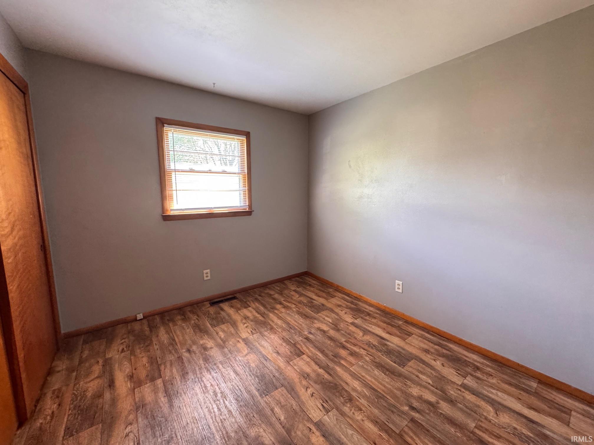 Room featuring wood-finish flooring, a single window with wood trim, and neutral-toned wall paint
