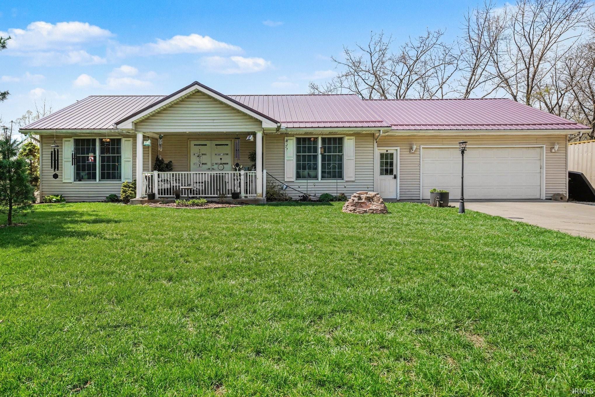 Ranch-style residence featuring a metal roof, light-colored siding, an attached garage, a covered front porch, and a well-maintained lawn