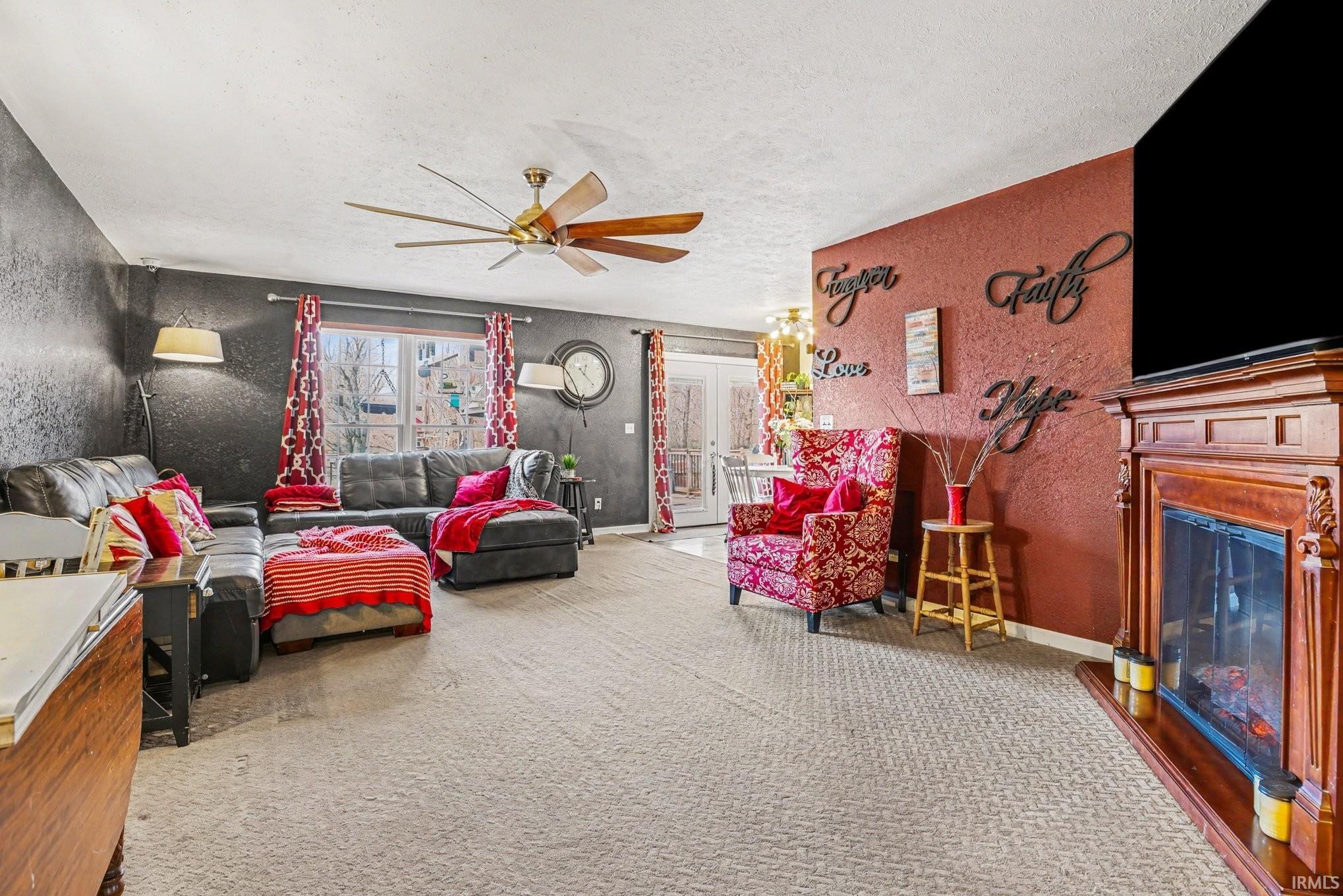 Spacious living area featuring carpet flooring, a ceiling fan with wood-finish blades, and a decorative fireplace with a substantial wood mantel