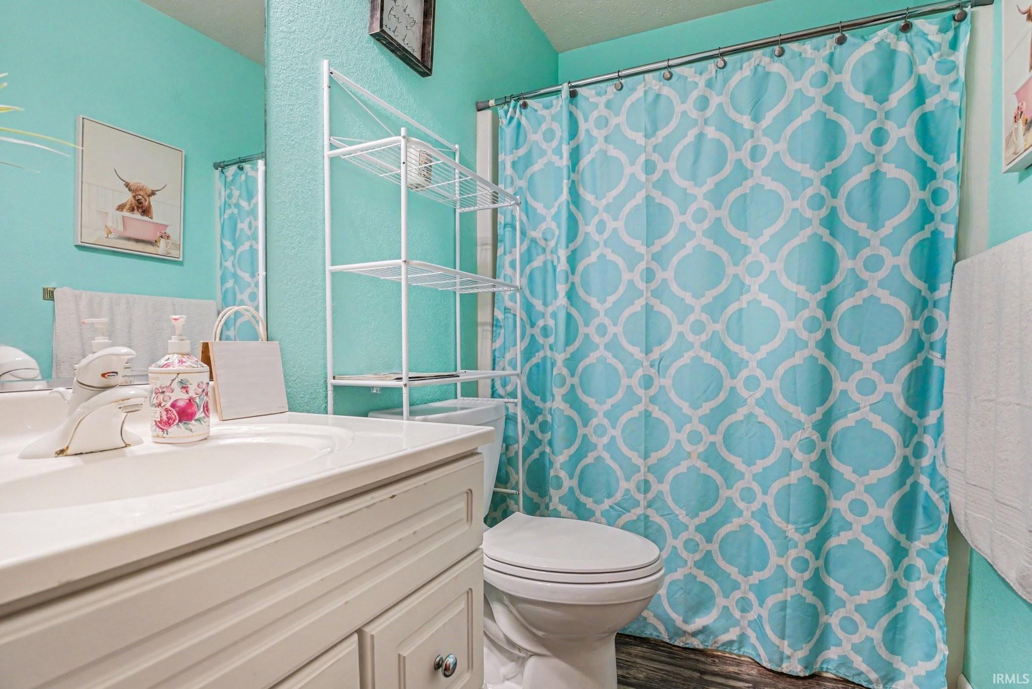 Bathroom featuring a white vanity with integrated sink, a toilet, and a shower area with a curtain