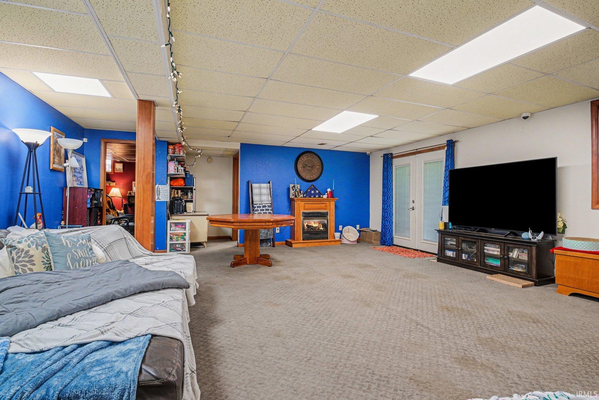 Spacious finished basement featuring carpet flooring, drop ceiling with integrated lighting, and a prominent fireplace with a wood mantle