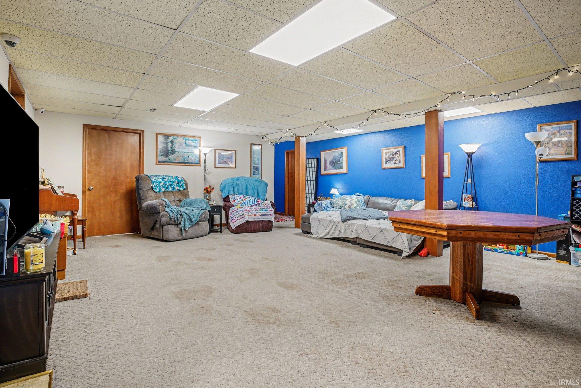 Spacious lower-level room featuring carpet flooring, drop ceiling with integrated lighting, and a neutral color palette with an accent wall