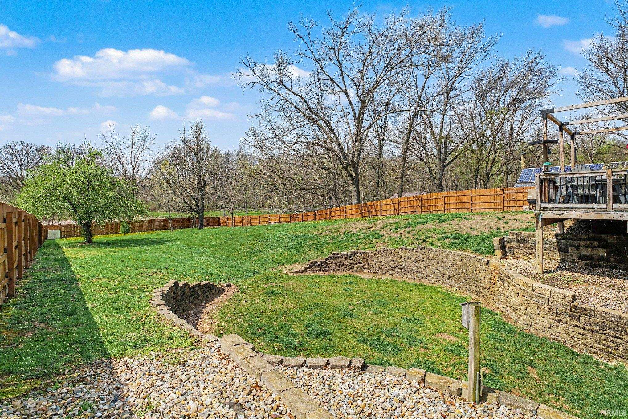 Expansive tiered backyard featuring stone retaining walls, a wood privacy fence, and a generous grass area