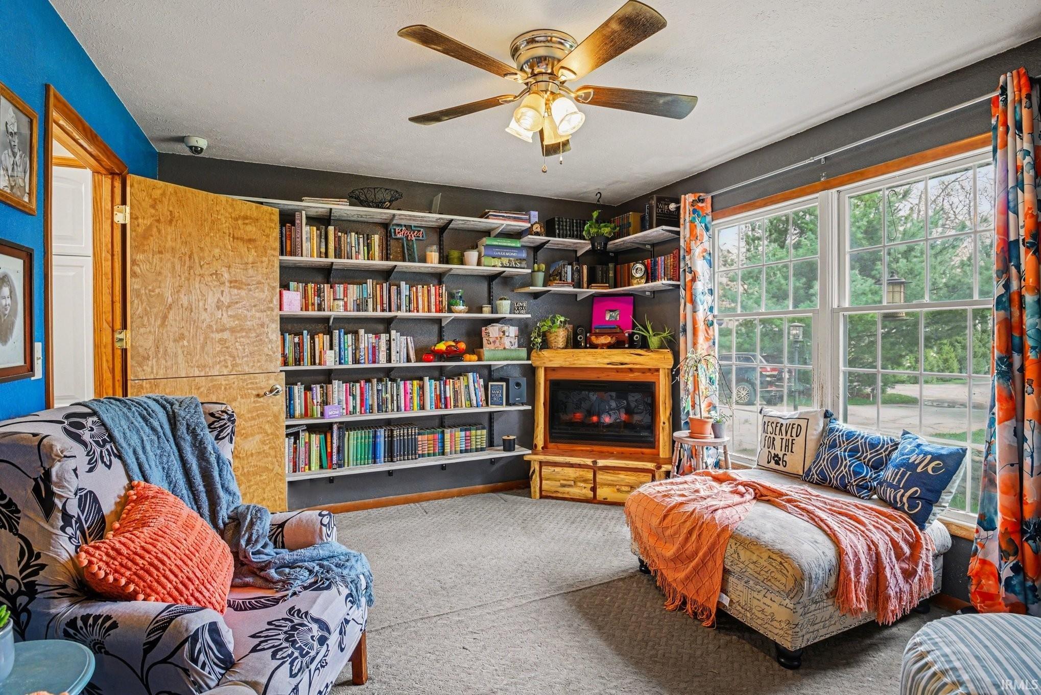 Living area featuring abundant natural light from large windows, built-in shelving, a wood-finish electric fireplace, and a ceiling fan
