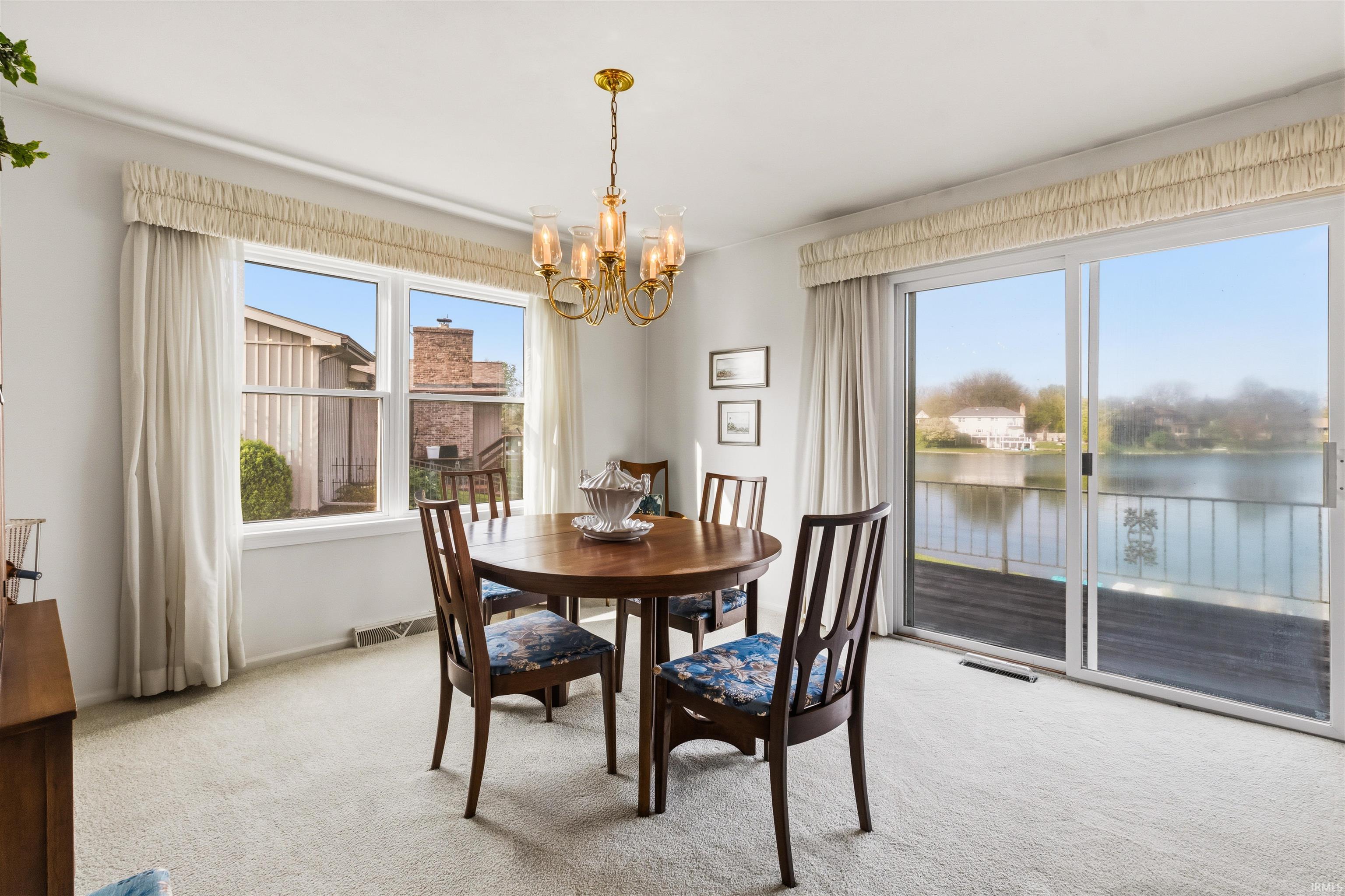 Spacious room with plush carpeting, featuring a brass chandelier, a large window, and sliding glass doors leading to a waterside balcony