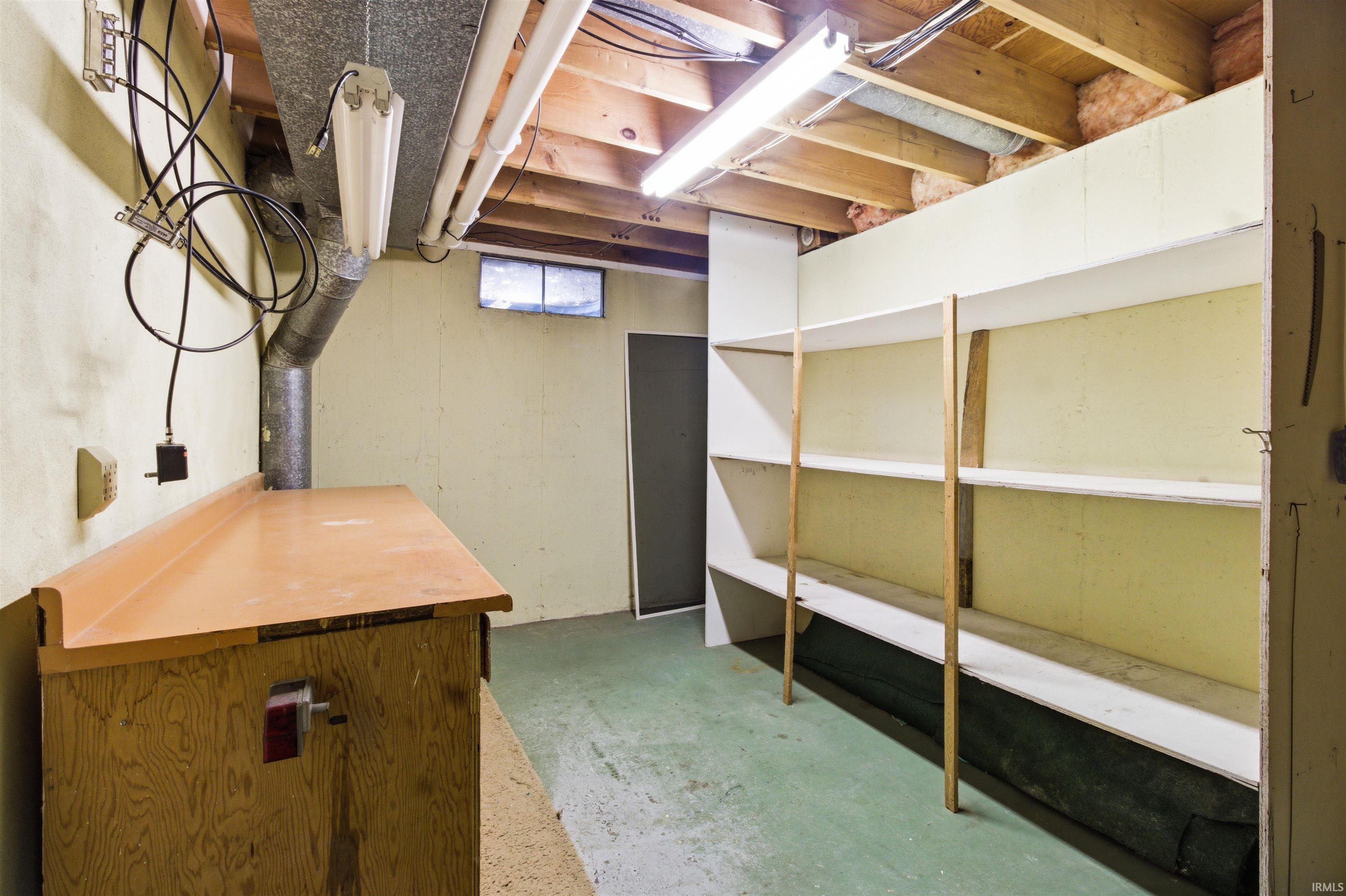 Utility space featuring built-in shelving, a workbench, exposed ceiling joists, and concrete flooring
