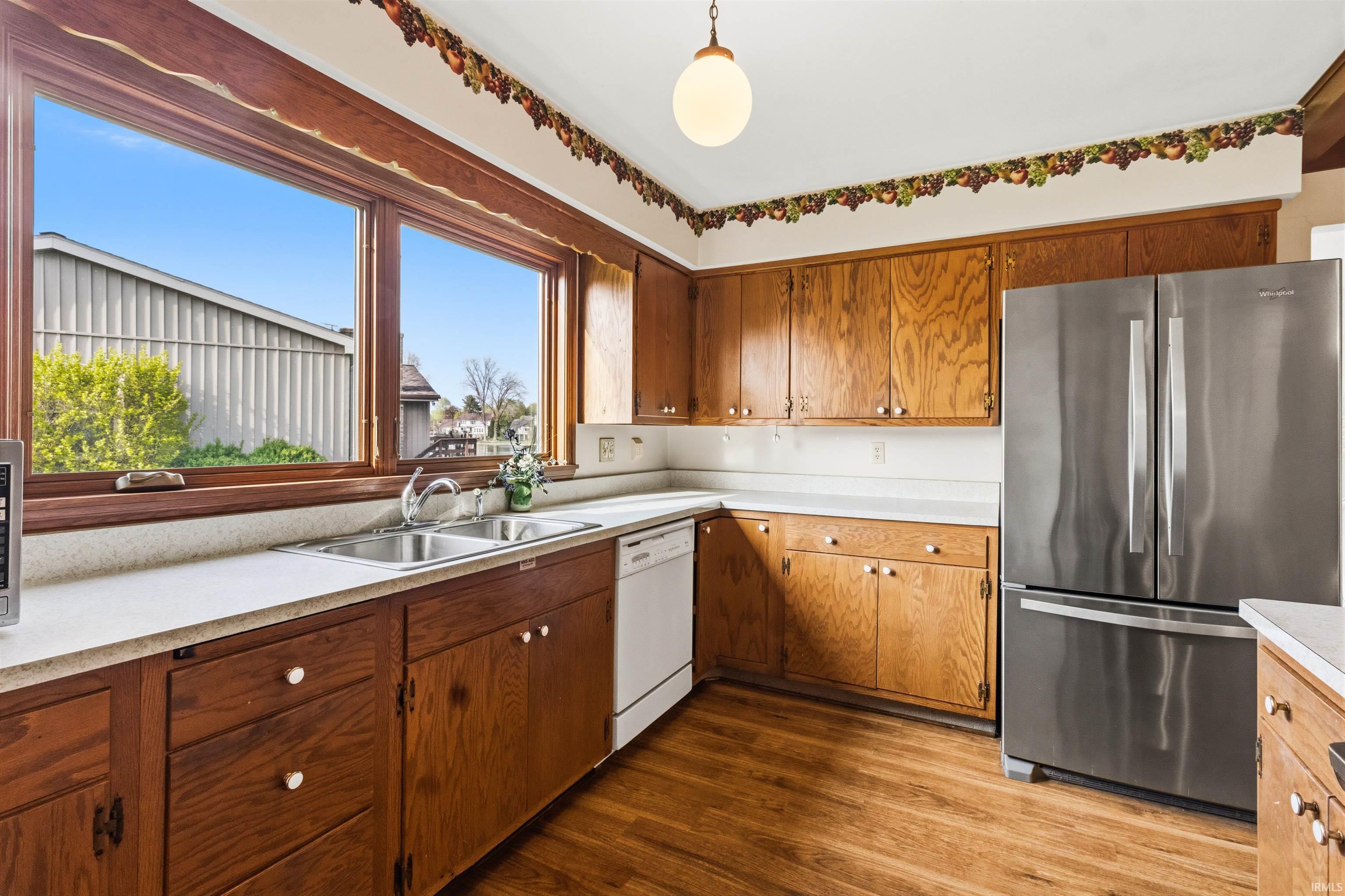 Kitchen featuring wood-finish flooring, wood cabinetry with white countertops, a stainless steel refrigerator, and an integrated double basin sink