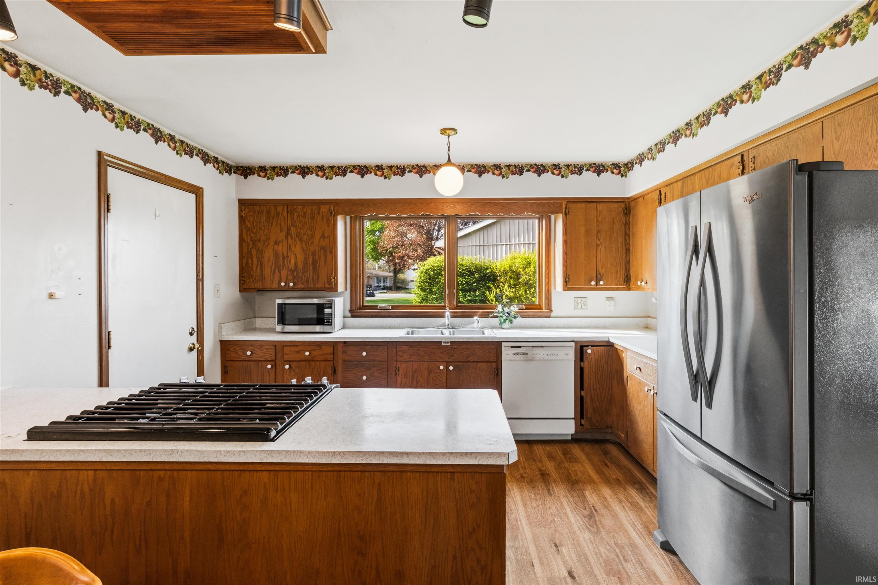 Kitchen featuring wood-finish flooring, wood cabinetry, white countertops, and a built-in cooktop on the island