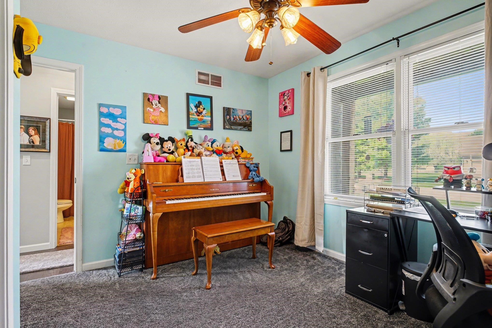 Carpeted room featuring a ceiling fan with light fixture, dual windows with blinds, and a doorway leading to an adjoining space