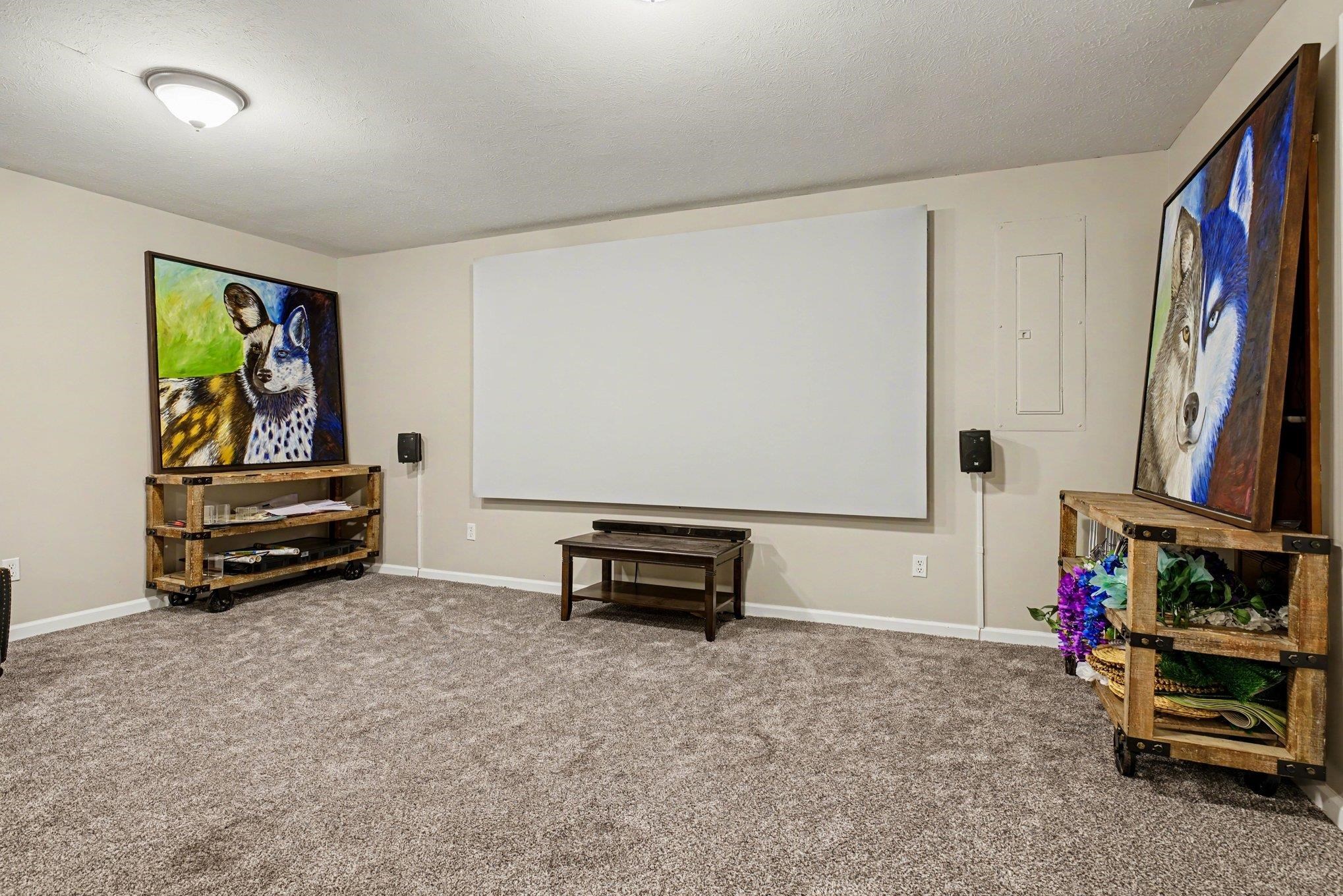 Spacious room featuring a large projector screen, wall-mounted speakers, and recessed ceiling lighting