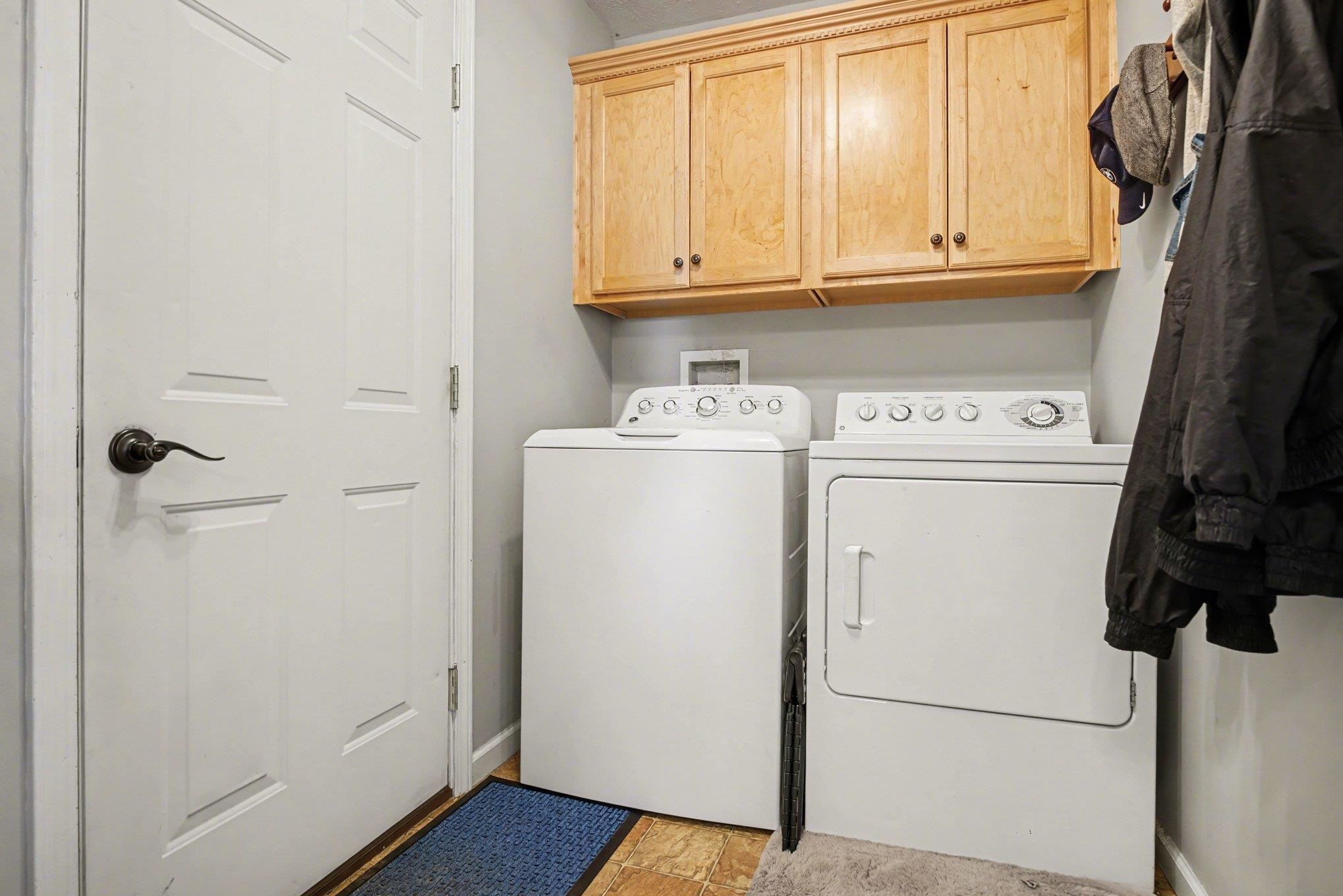 Dedicated laundry area featuring wood-finish flooring, light gray wall paint, and overhead wood cabinetry with decorative crown molding