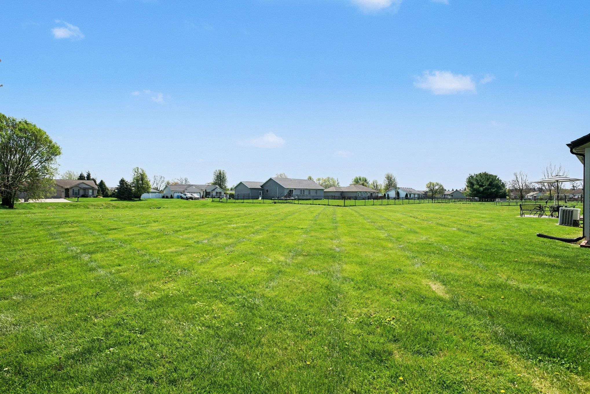 Expansive green lawn with a partial black wire fence defining the rear property line