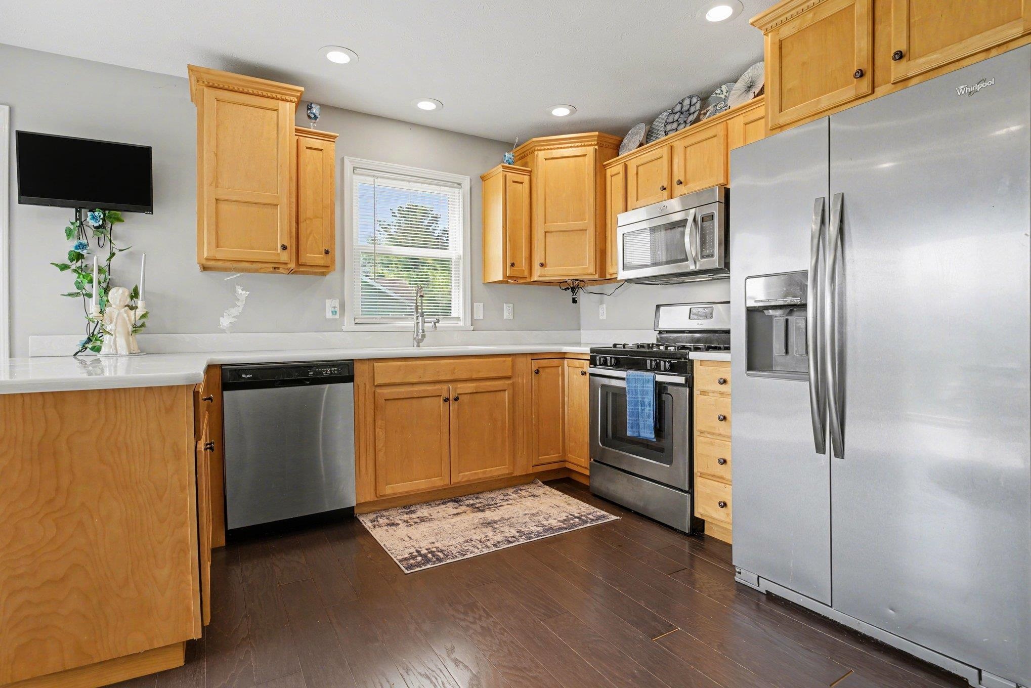 Kitchen featuring wood cabinetry, stainless steel appliances, white countertops, and dark wood-finish flooring
