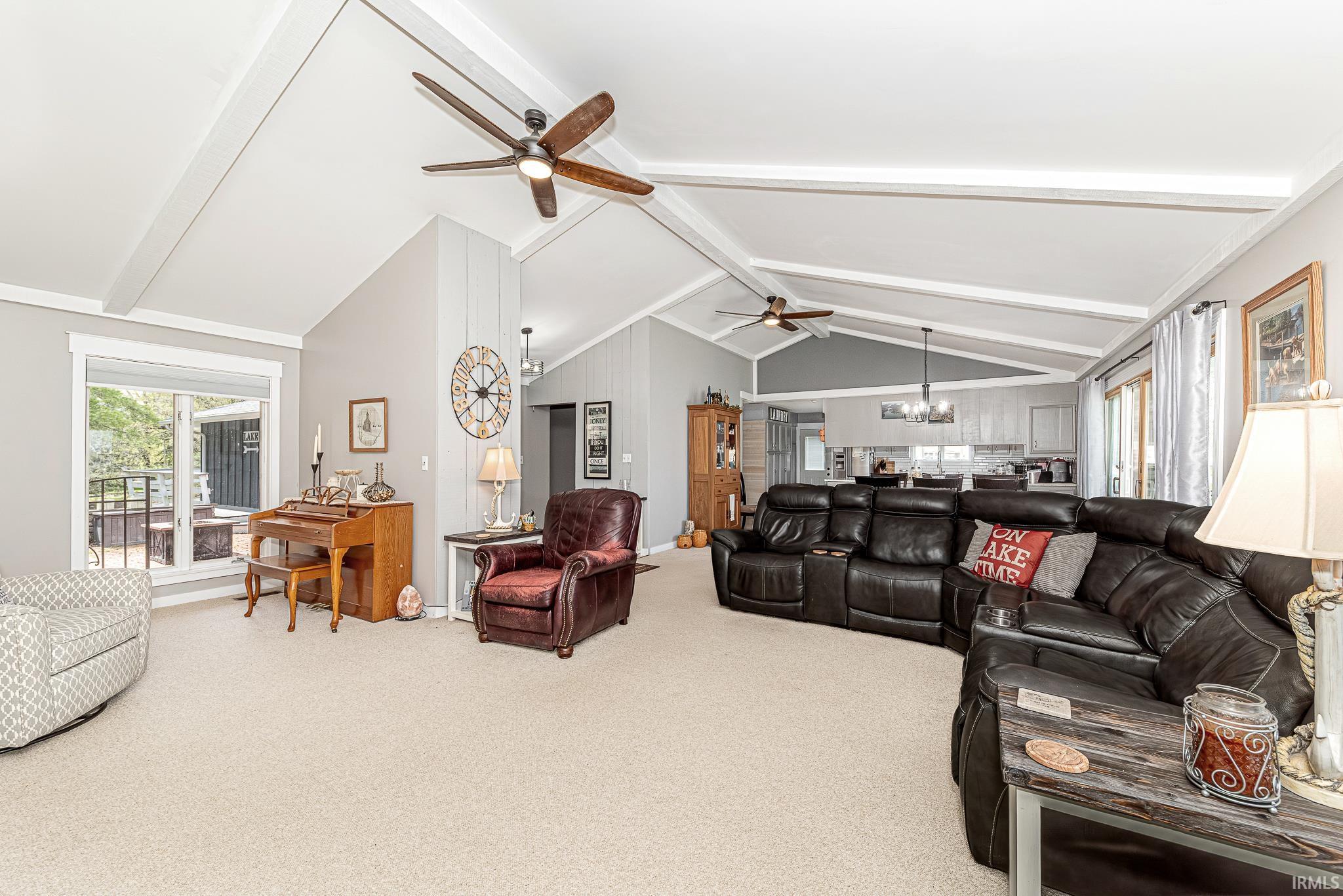 Expansive open-concept living area featuring vaulted ceilings with exposed beams, multiple ceiling fans, and neutral-toned carpeting
