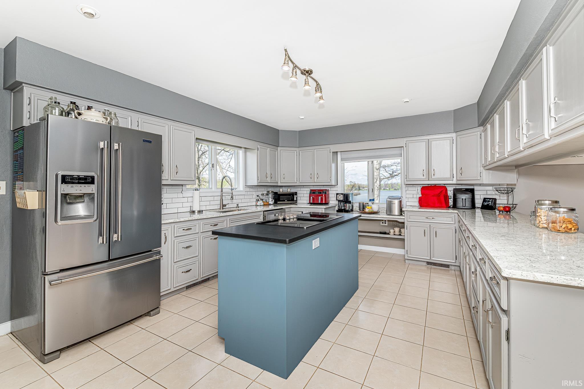 Modern kitchen featuring a central island with a dark countertop, extensive light-toned cabinetry, light-toned tile flooring, and a stainless steel French door refrigerator