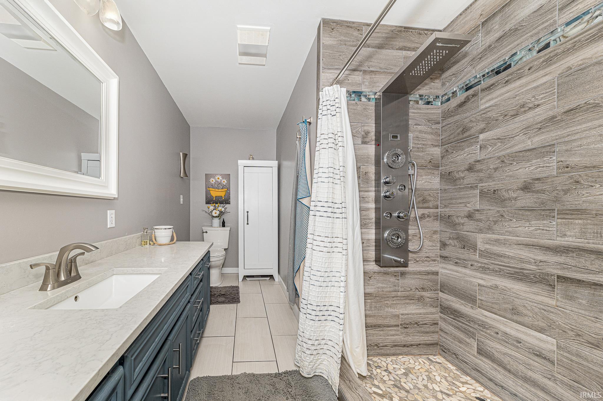 Shower with wood-look tile surround and pebble flooring, complemented by a multi-function shower panel