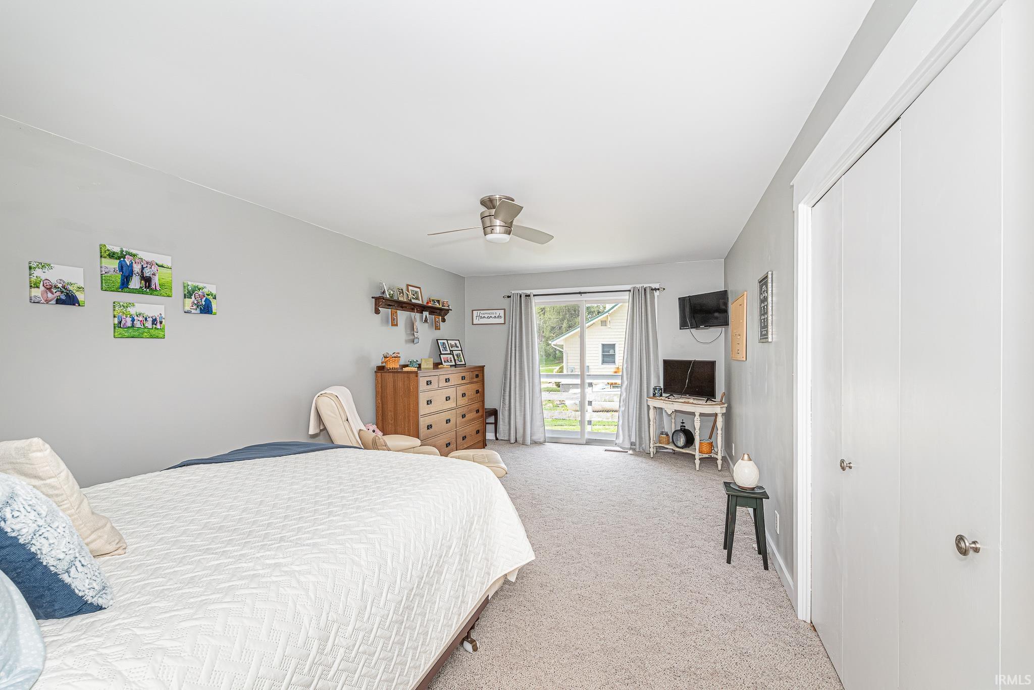 Spacious bedroom featuring light gray walls, plush carpeting, a ceiling fan with integrated lighting, and a sliding glass door providing exterior access