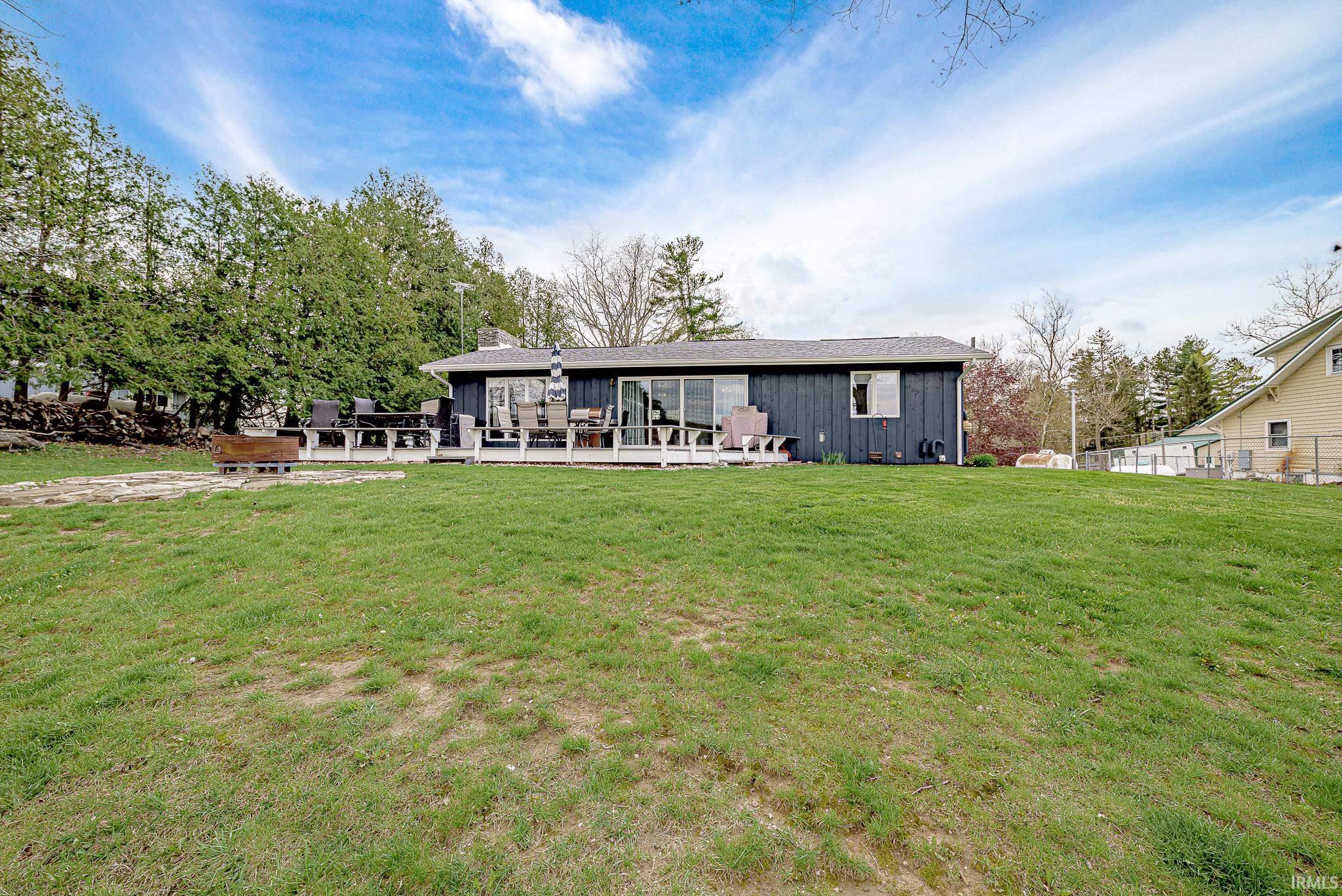 Expansive lawn area with a dark-sided single-story residence featuring a white deck with a glass railing and a sliding glass door