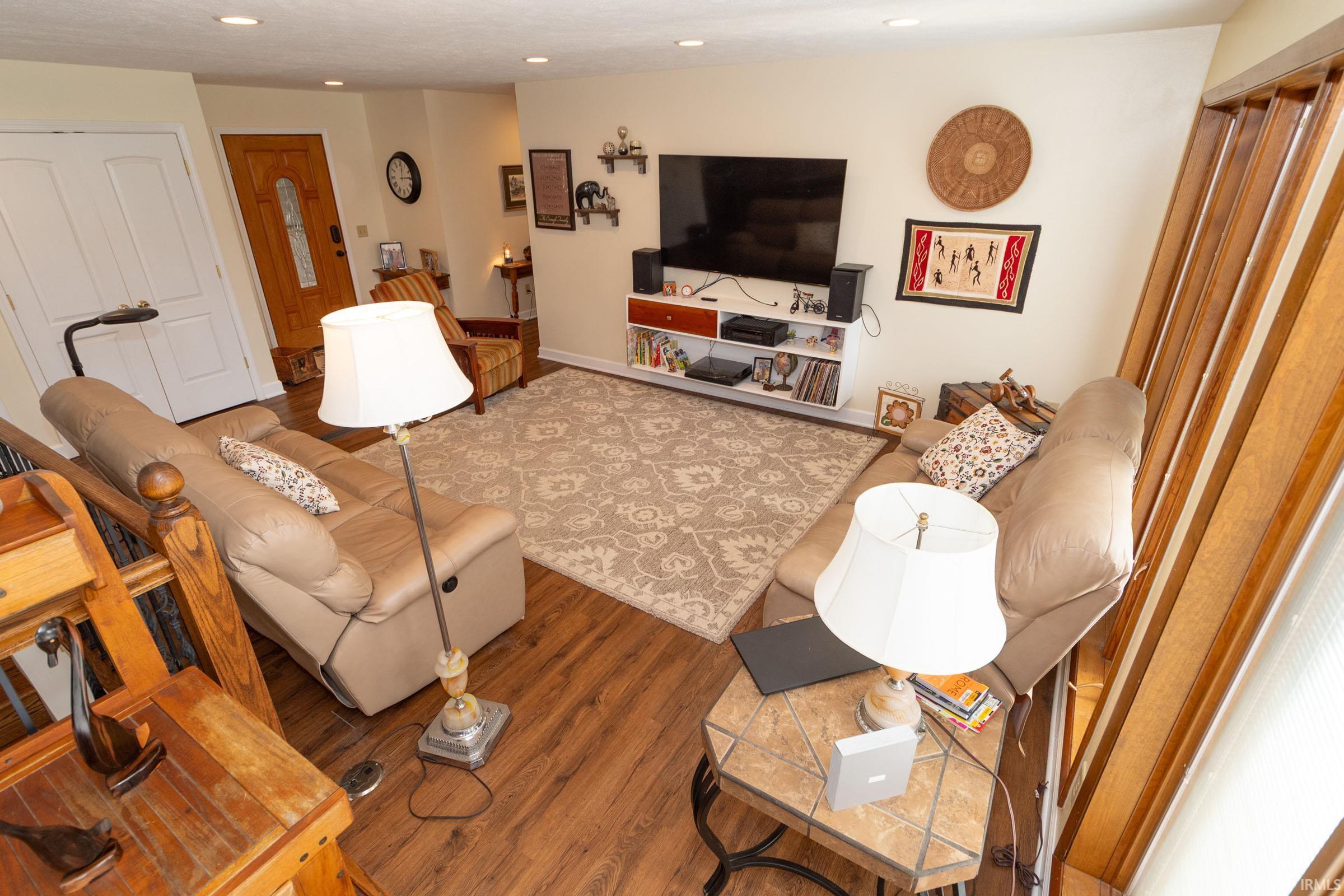 Open living area featuring wood-finish flooring, recessed lighting, and a white paneled entry door
