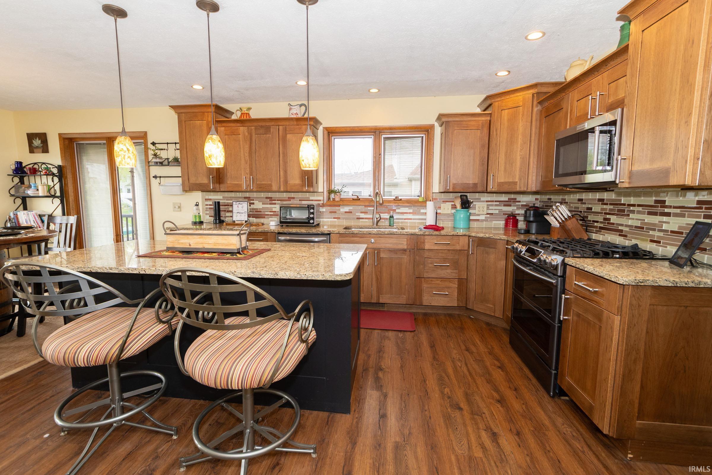 Kitchen featuring a central island with a granite countertop, pendant lighting, wood-finish flooring, recessed lighting, and ample wood cabinetry
