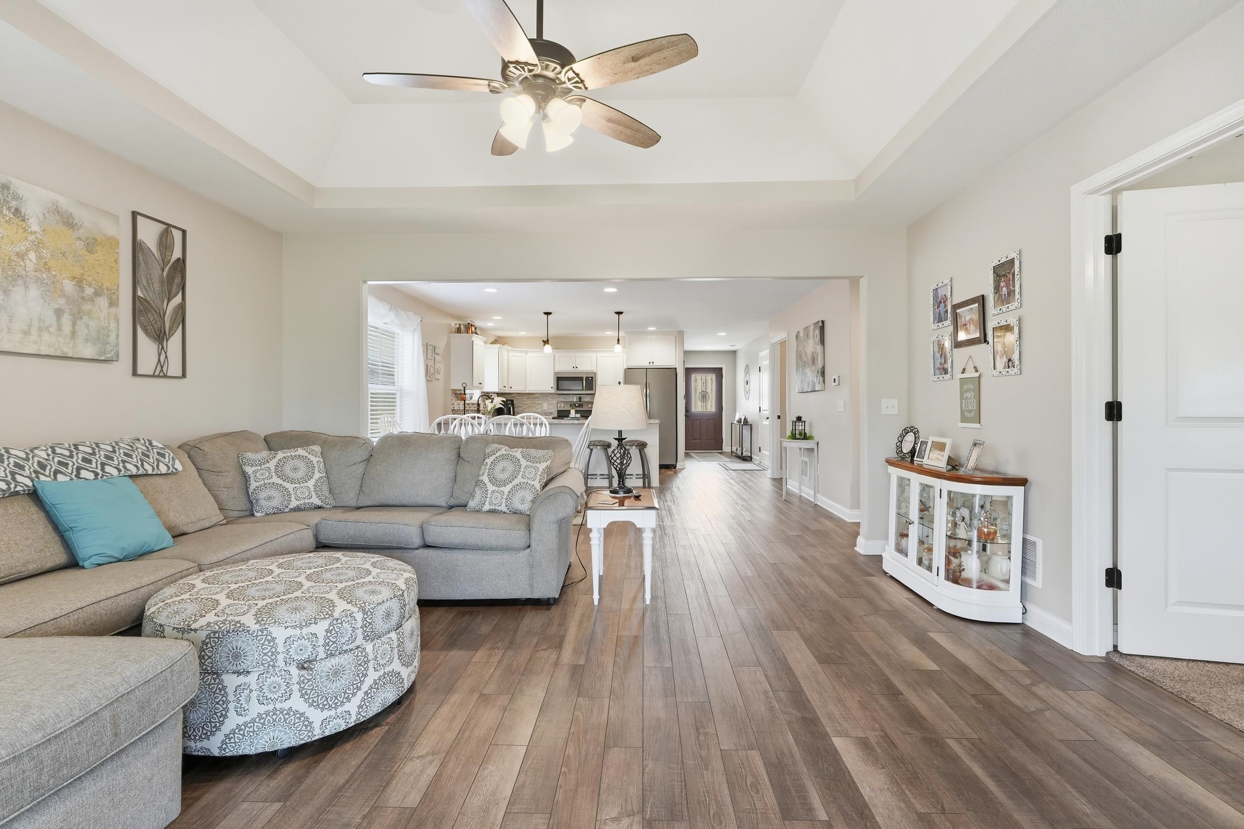 Spacious living area featuring wood-finish flooring, a tray ceiling with a ceiling fan, and recessed lighting