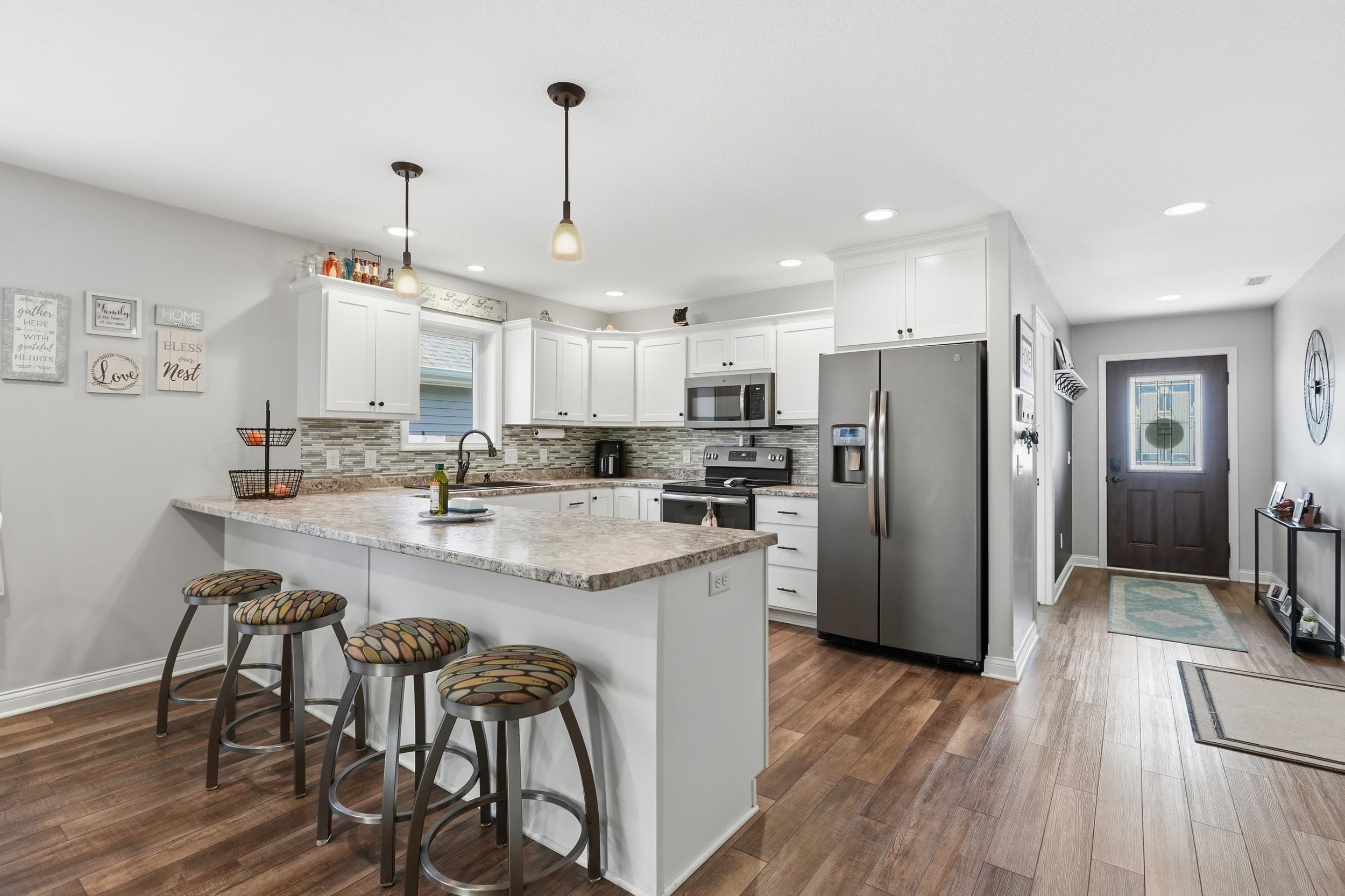 Open-concept kitchen featuring white cabinetry, stainless steel appliances, a breakfast bar, recessed lighting, and wood-finish flooring