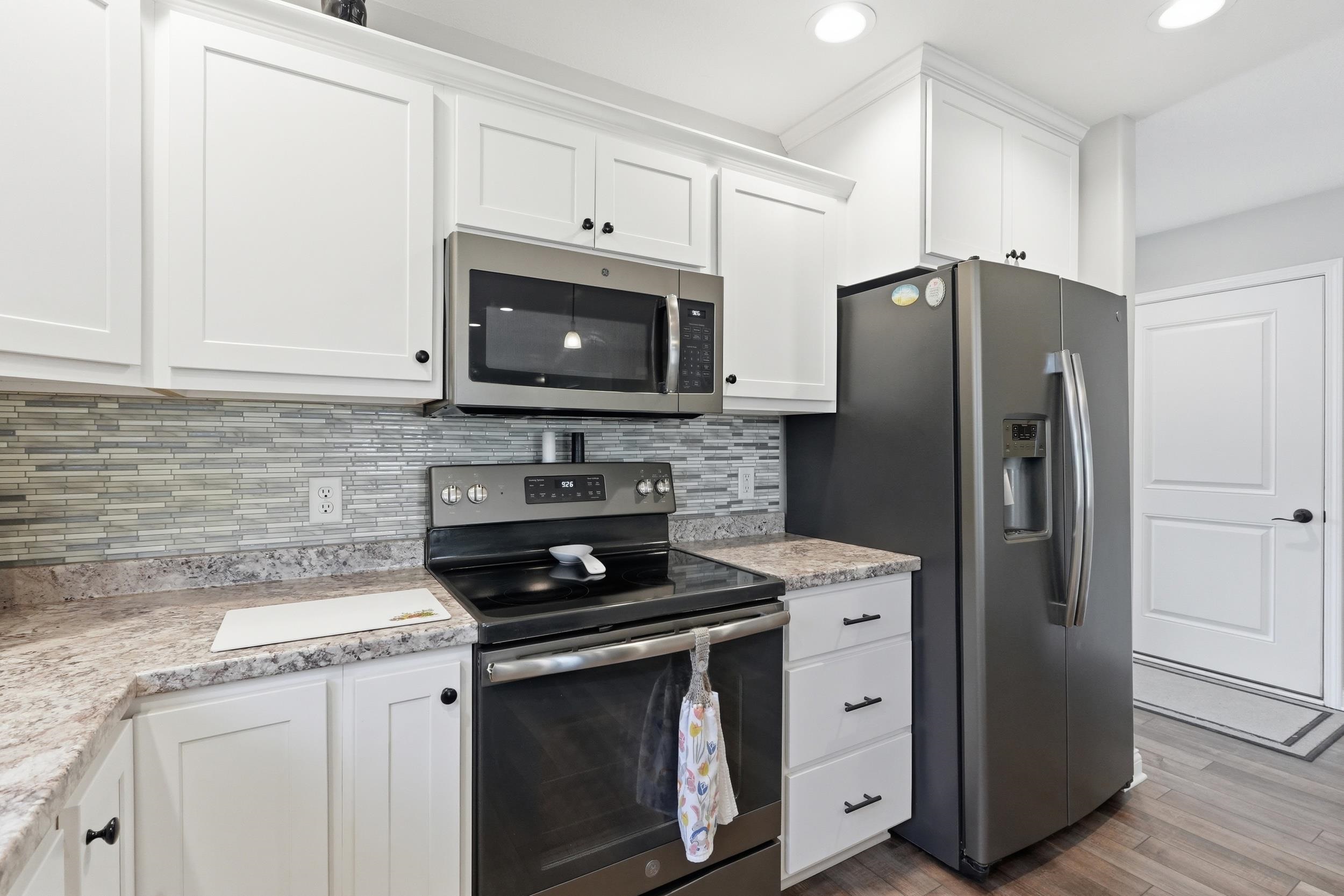 Kitchen featuring white shaker-style cabinetry with dark hardware, a stainless steel microwave, and a black range